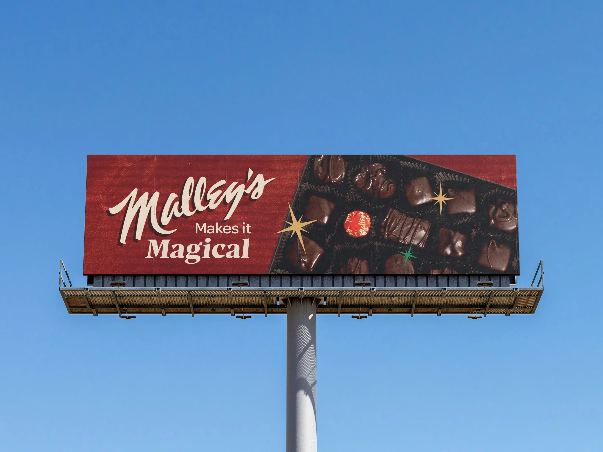 Billboard advertisement for Malley's chocolates with the text "Malley's Makes it Magical" and an image of assorted chocolates against a red background with star accents.