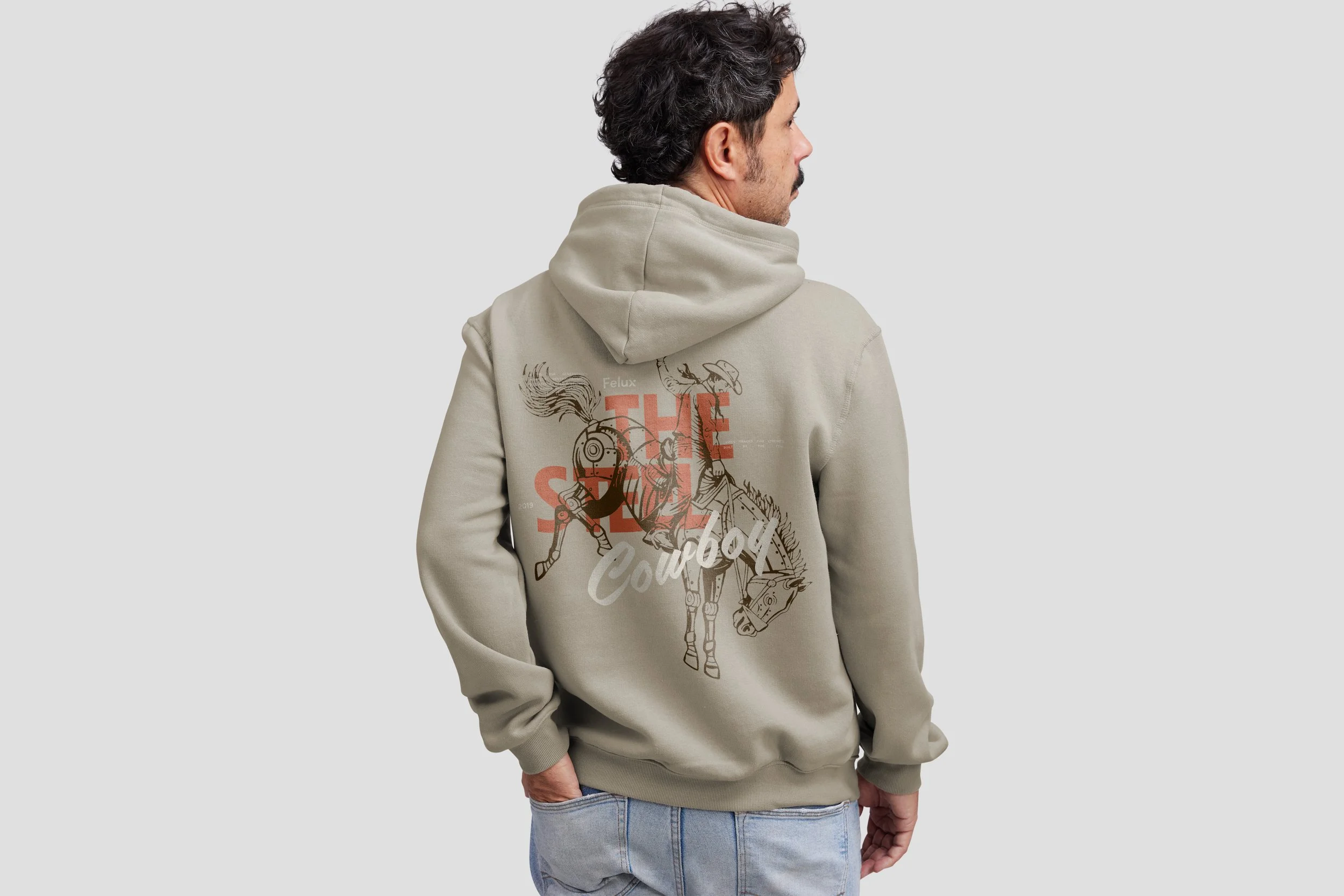 A man wearing a beige hoodie with a graphic design of a robotic horse and the words 'The Cowboy' on the back, standing against a plain light gray background.