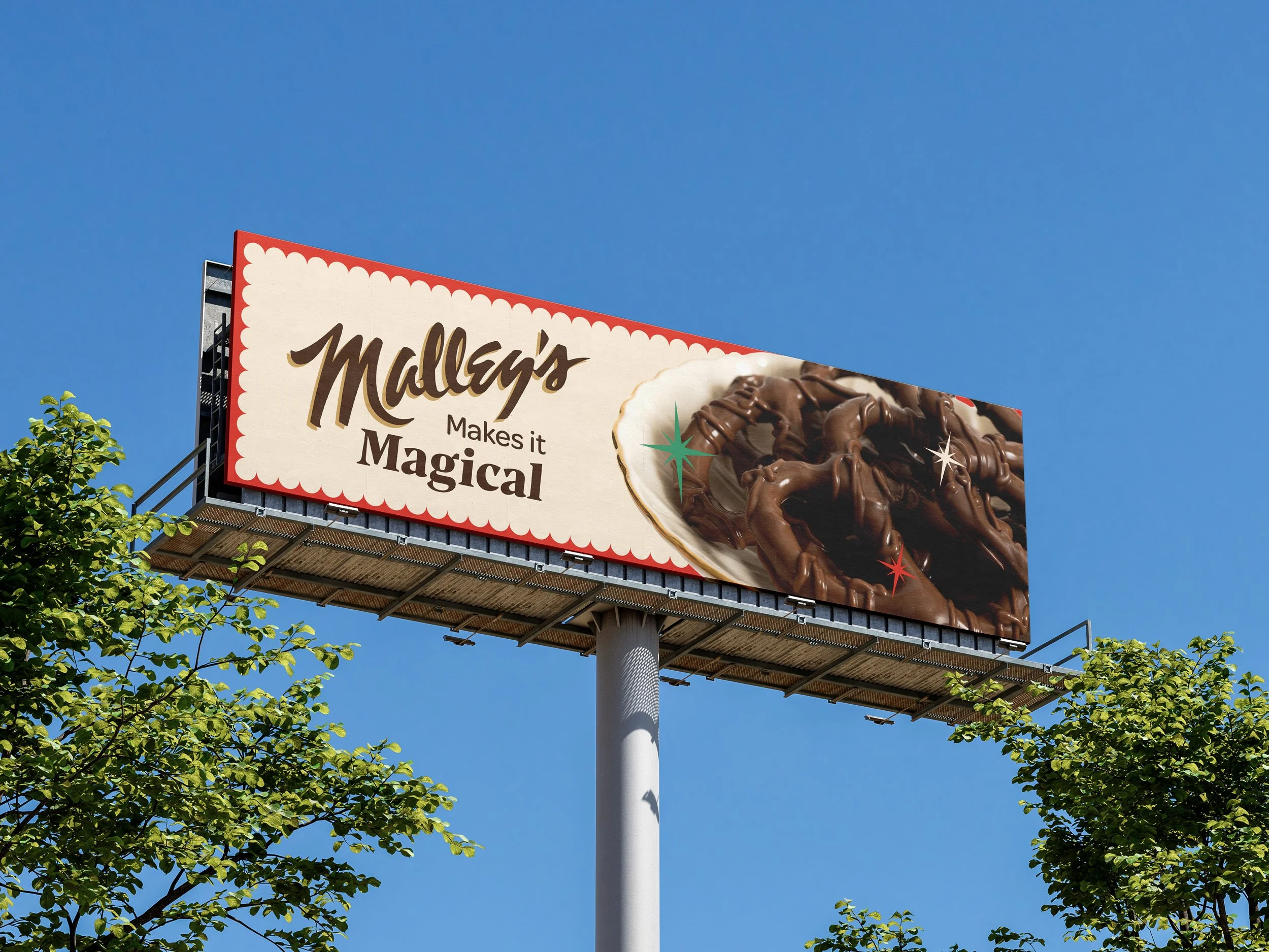 Billboard advertising Mallory's, featuring an image of chocolate-covered pretzels and the slogan 'Mallory's makes it magical' against a blue sky with green trees in the foreground.