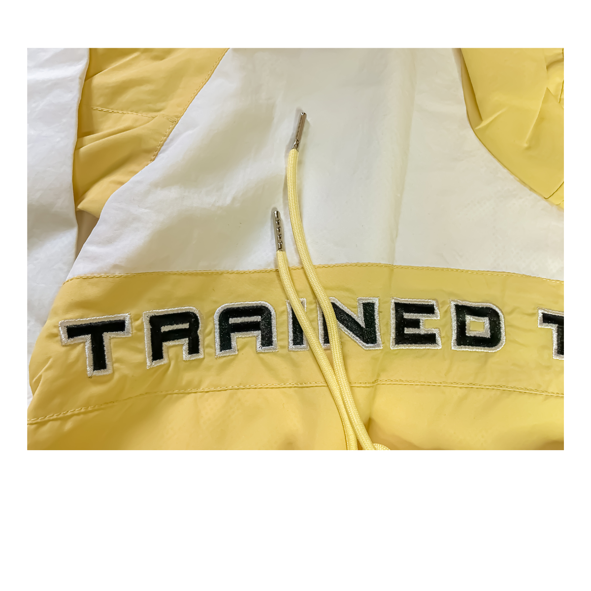 Close-up of a yellow jacket with black and white embroidered letters spelling 'TRAINED' on the front.
