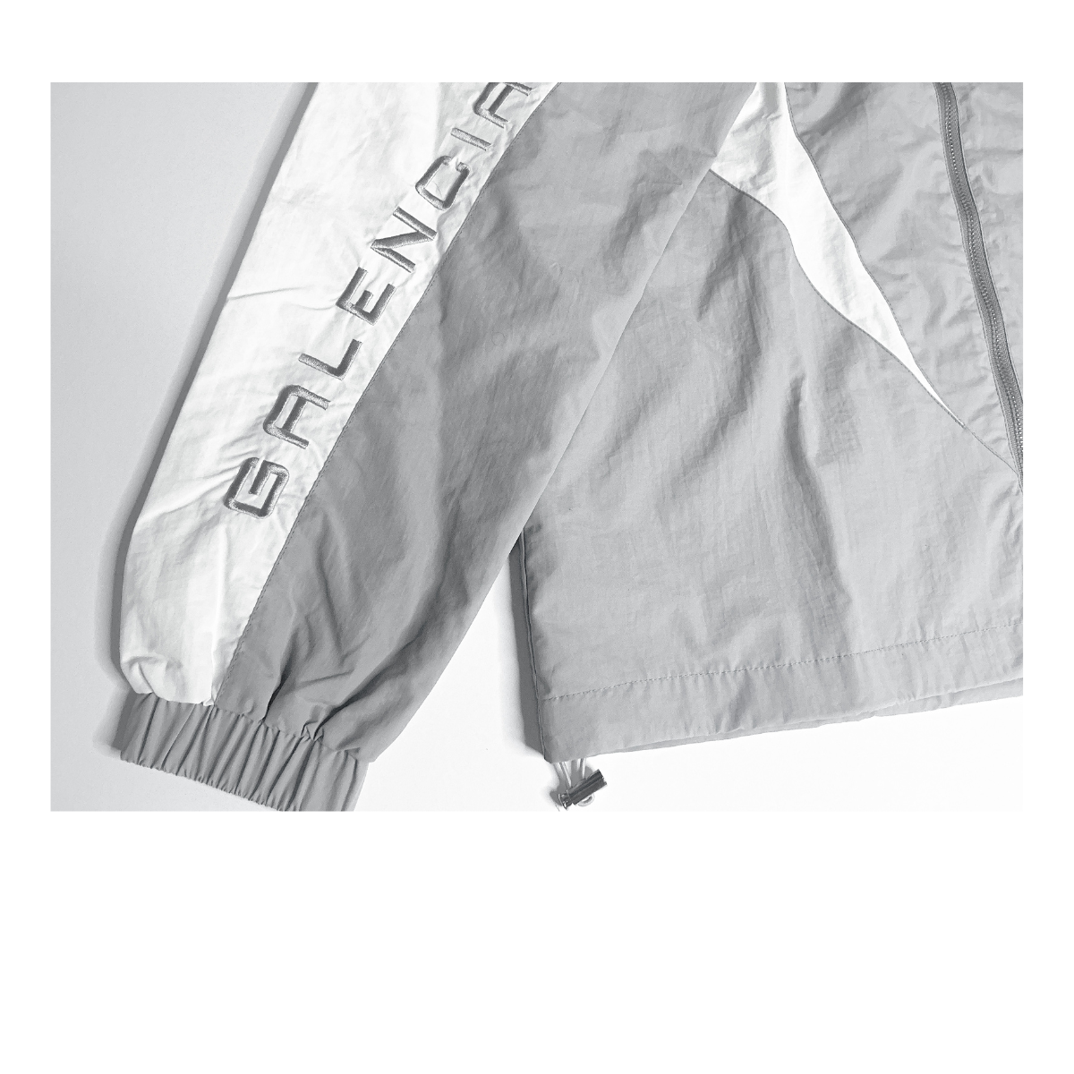 Gray jacket with white sleeve panel and embroidered text on the sleeve.