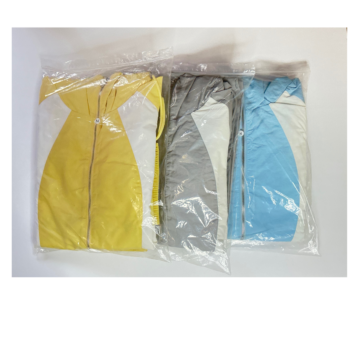 Three color-coded jackets in plastic bags: yellow, gray, and blue, out of their packaging.