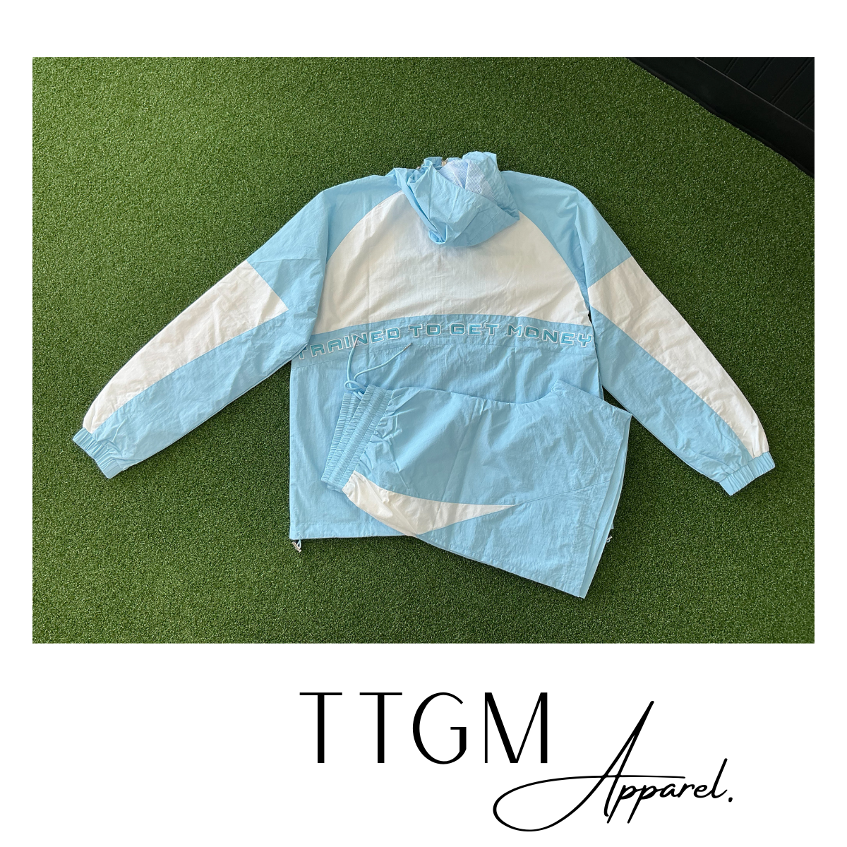 Light blue and white windbreaker jacket with the phrase "Trained to Get Money" embroidered on the front, with a white border and black logo text reading "TTGM Apparel".