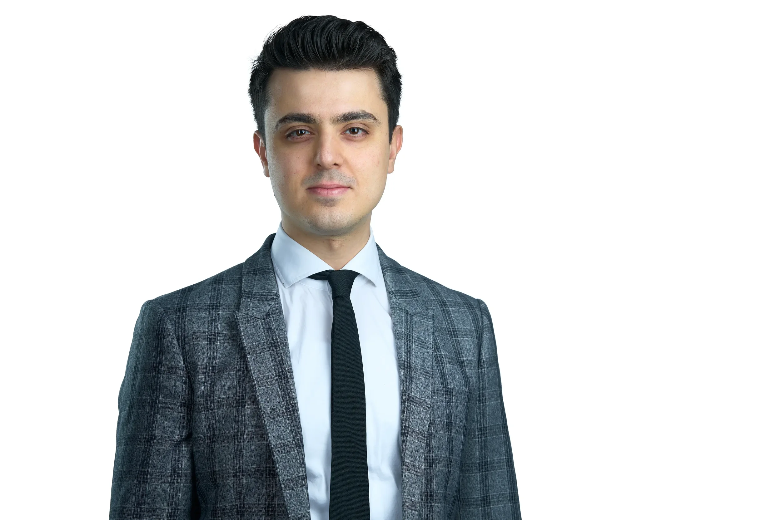 A young man in a gray plaid suit, white shirt, and black tie, standing against a plain white background.