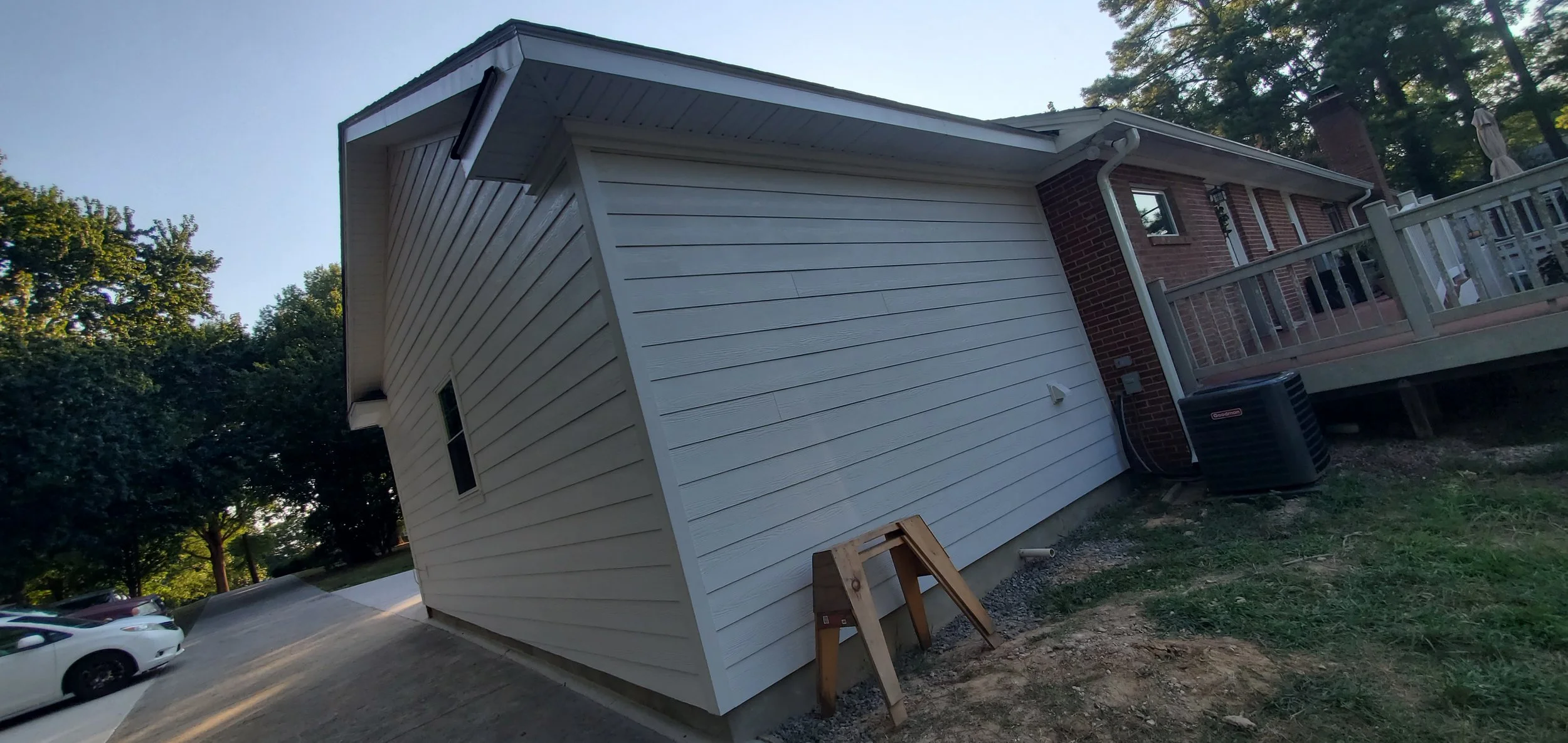 Side view of a residential house with white siding, a brick section, a deck, and an air conditioning unit on the ground.