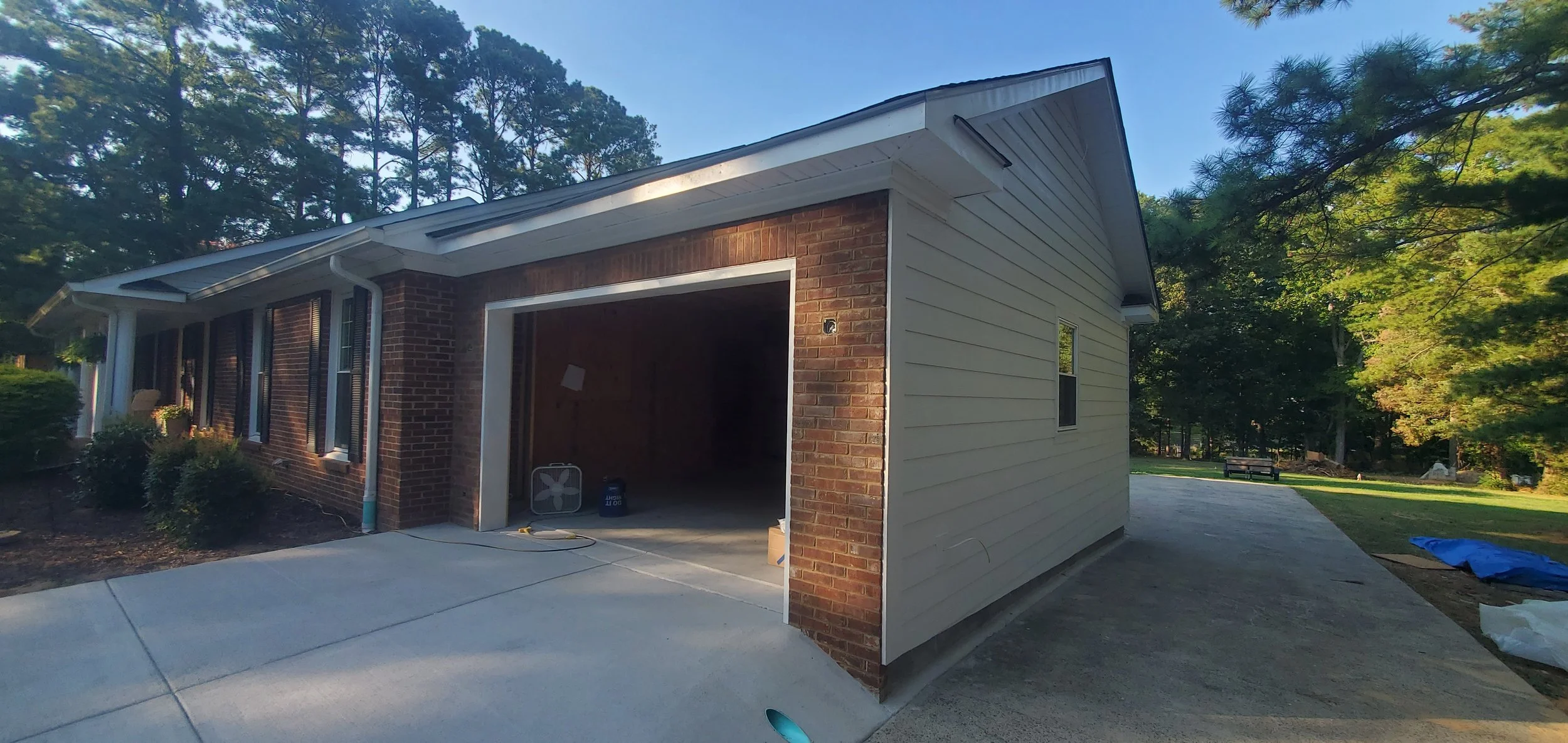 Residential house under construction with an open garage, surrounded by trees and a concrete driveway.
