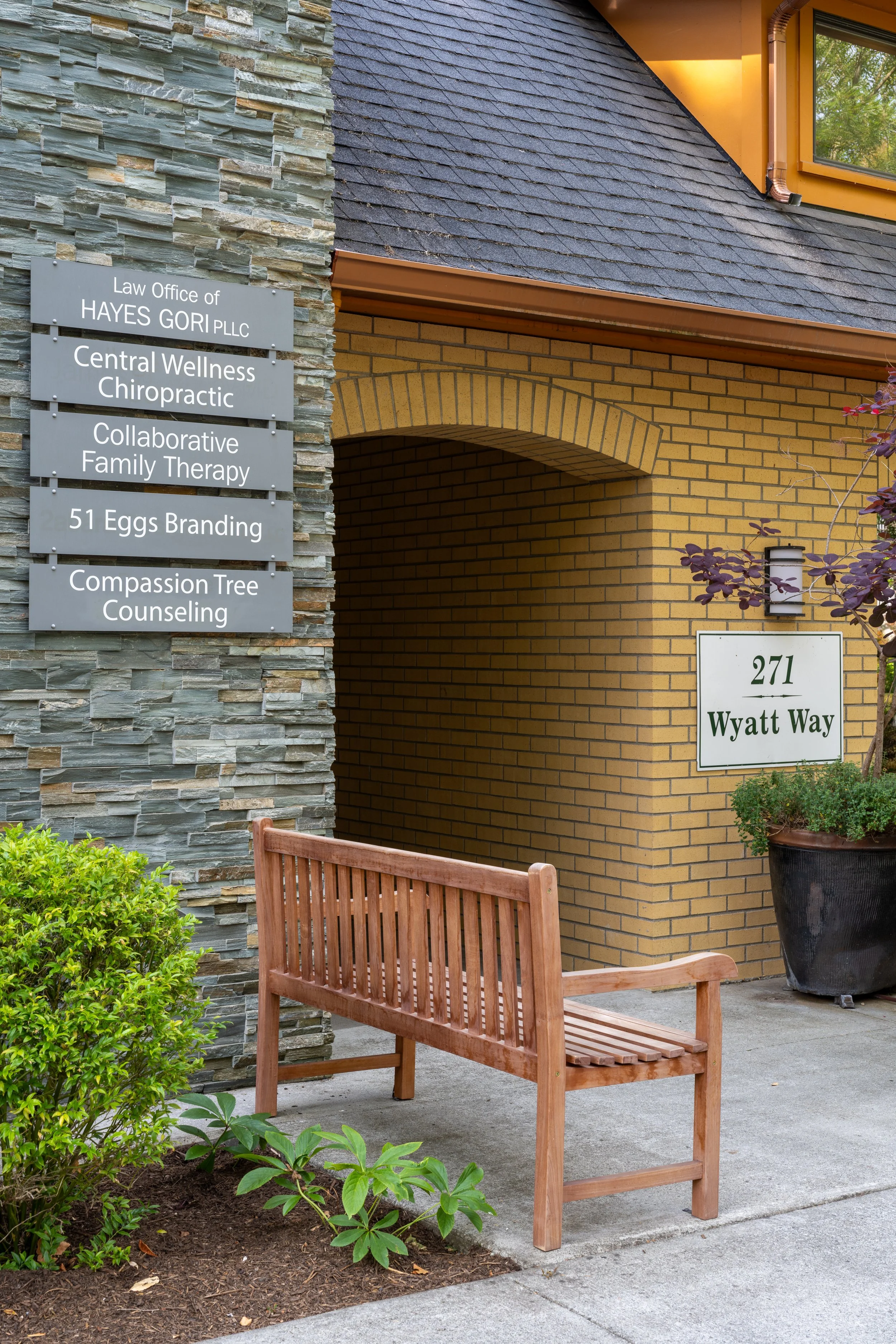 Street view of Compassion Tree Counseling on Bainbridge Island. A stone building with a bench and signs.
