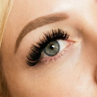 Close-up of a woman's eye with long, thick eyelash extensions and well-defined eyebrow.