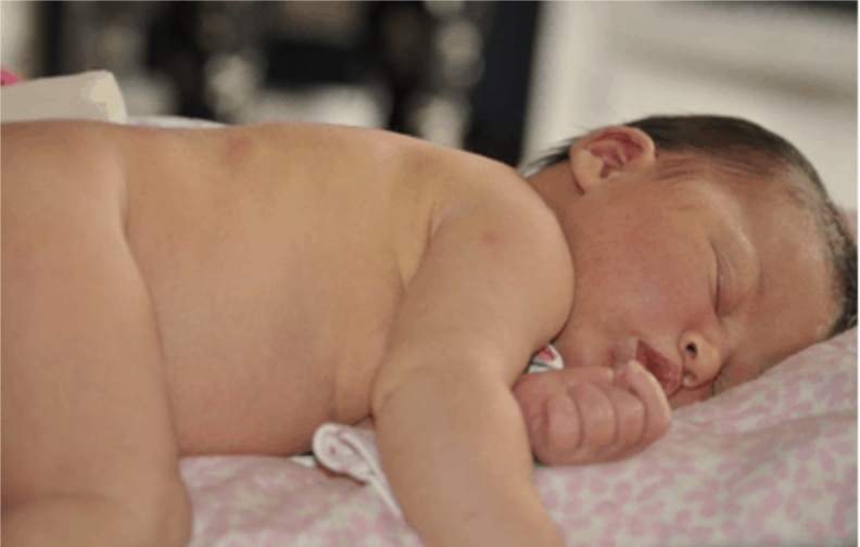A newborn baby sleeps on a pink and white patterned blanket.