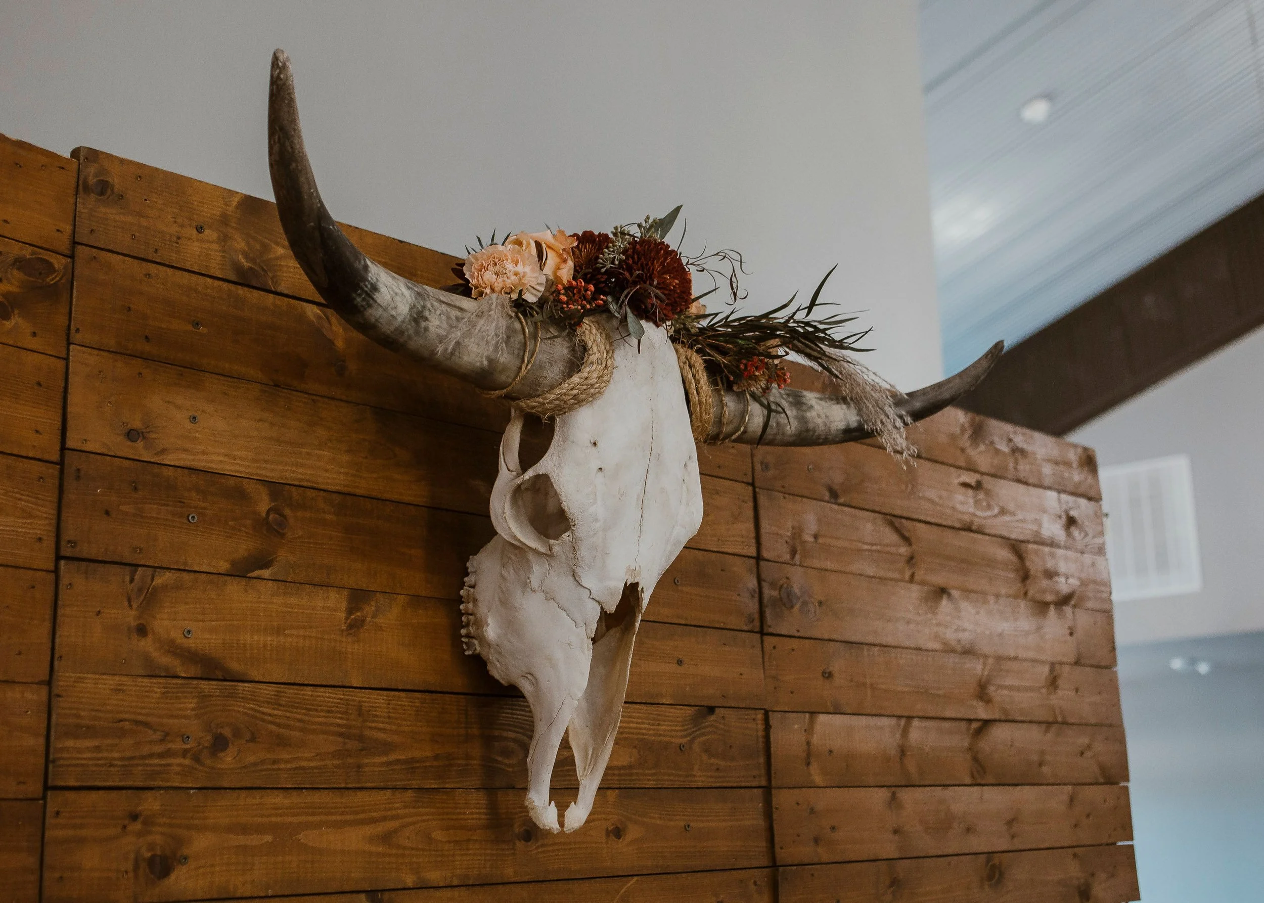 Decorative bull skull mounted on a wooden wall with dried flowers and foliage on its horns.