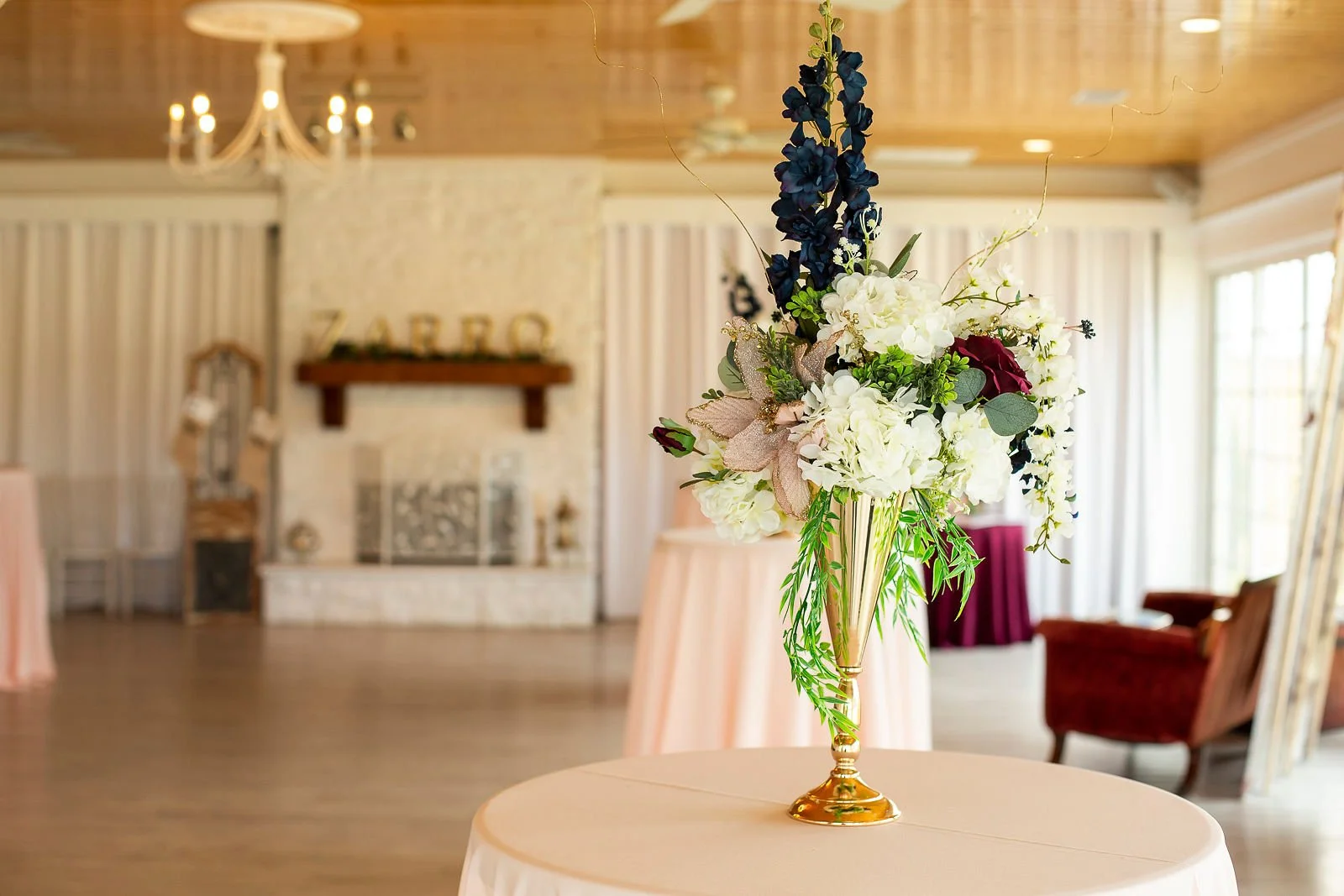 Elegant floral centerpiece with white, purple, and burgundy flowers on a round table in a decorated indoor venue.