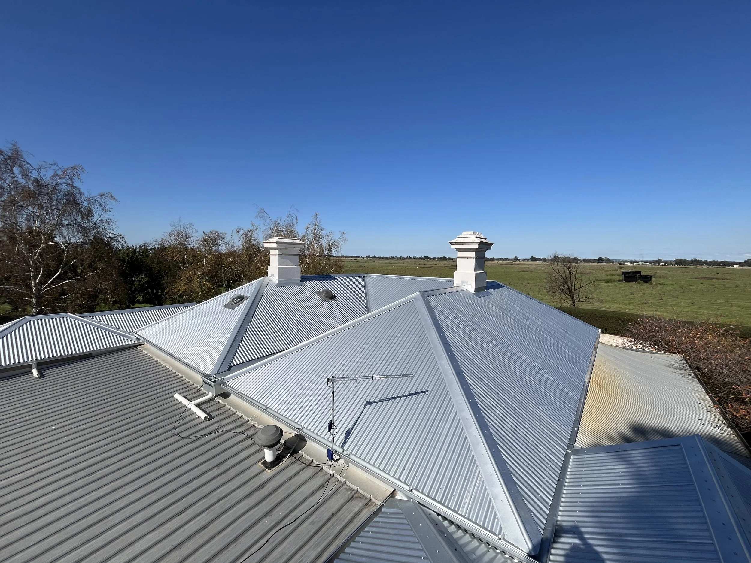 View of a metal roof on a rural building with a vast open field and blue sky in the background.