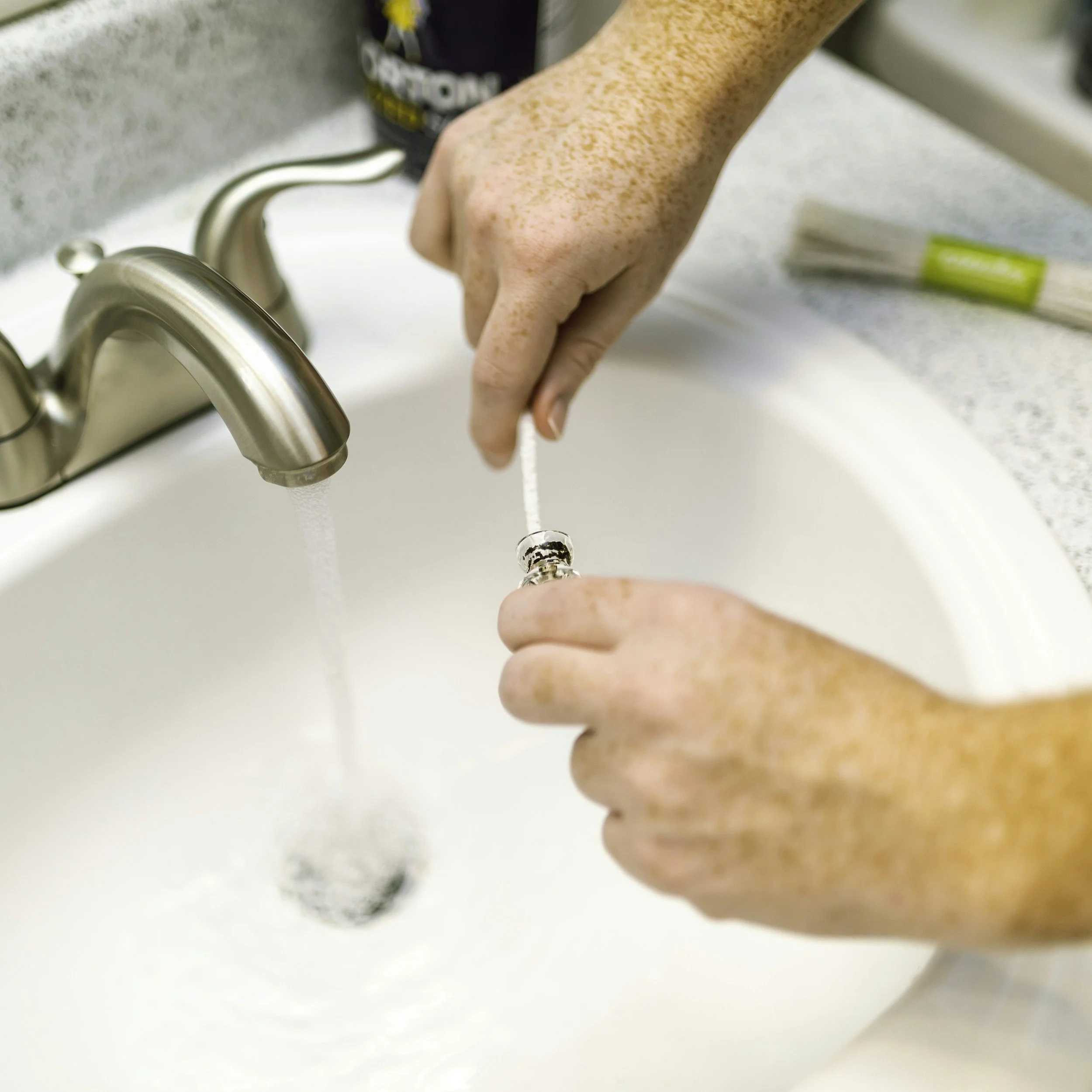 Hands holding a necklace under running water in a kitchen sink.