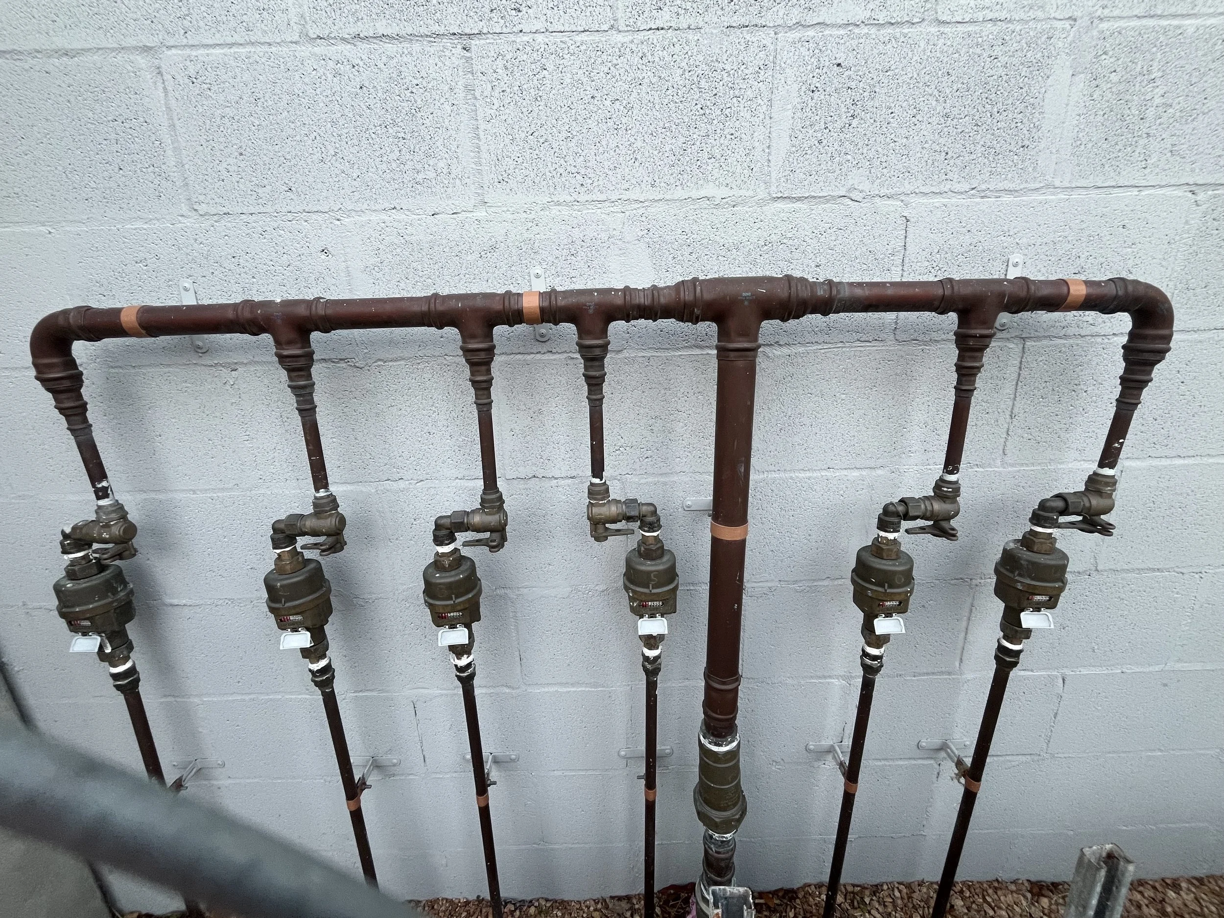 A plumbing system with multiple pipes and valves mounted against a cinder block wall.