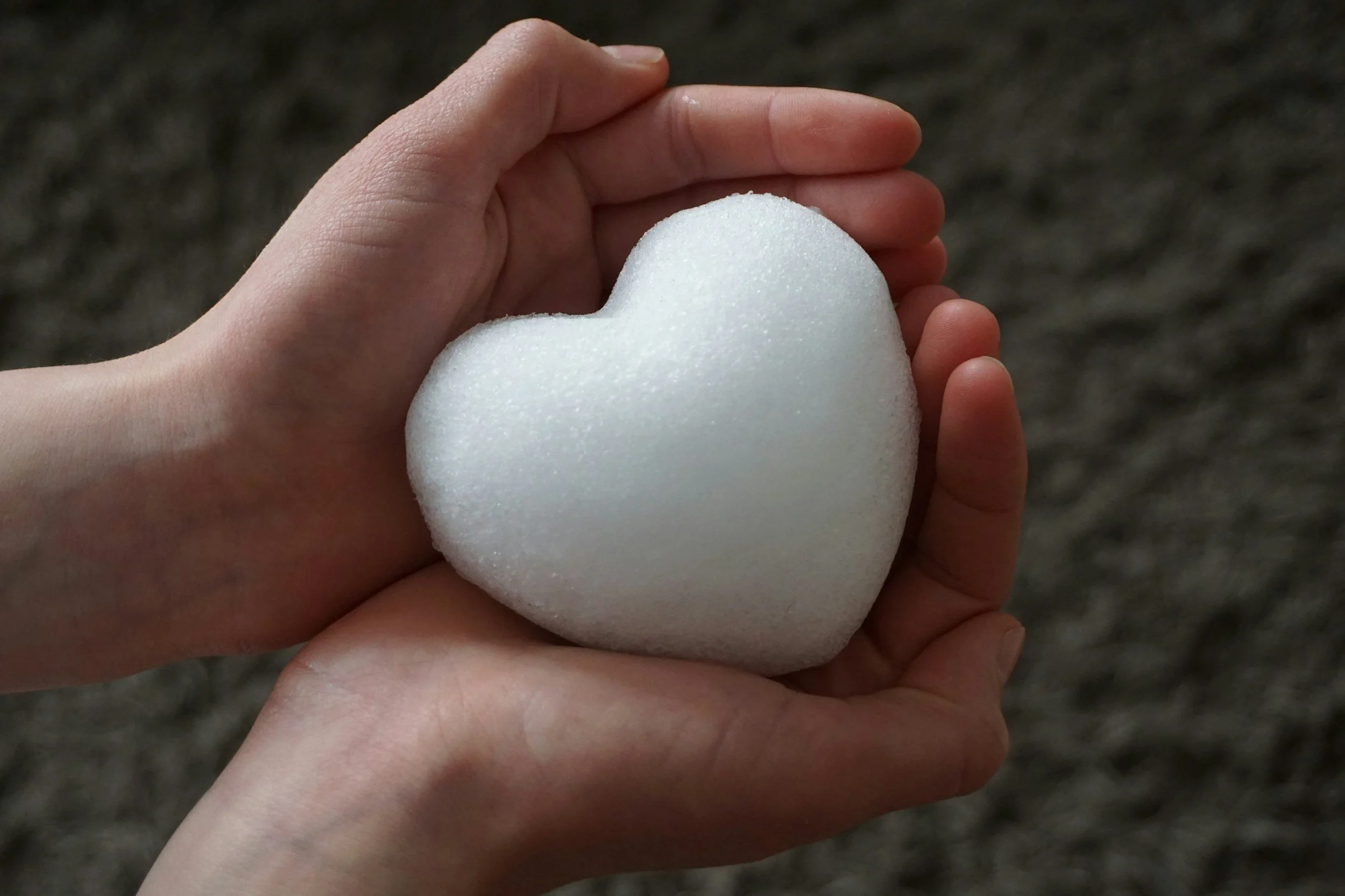 A person's hand holding a white heart-shaped object, with a dark, blurred background.