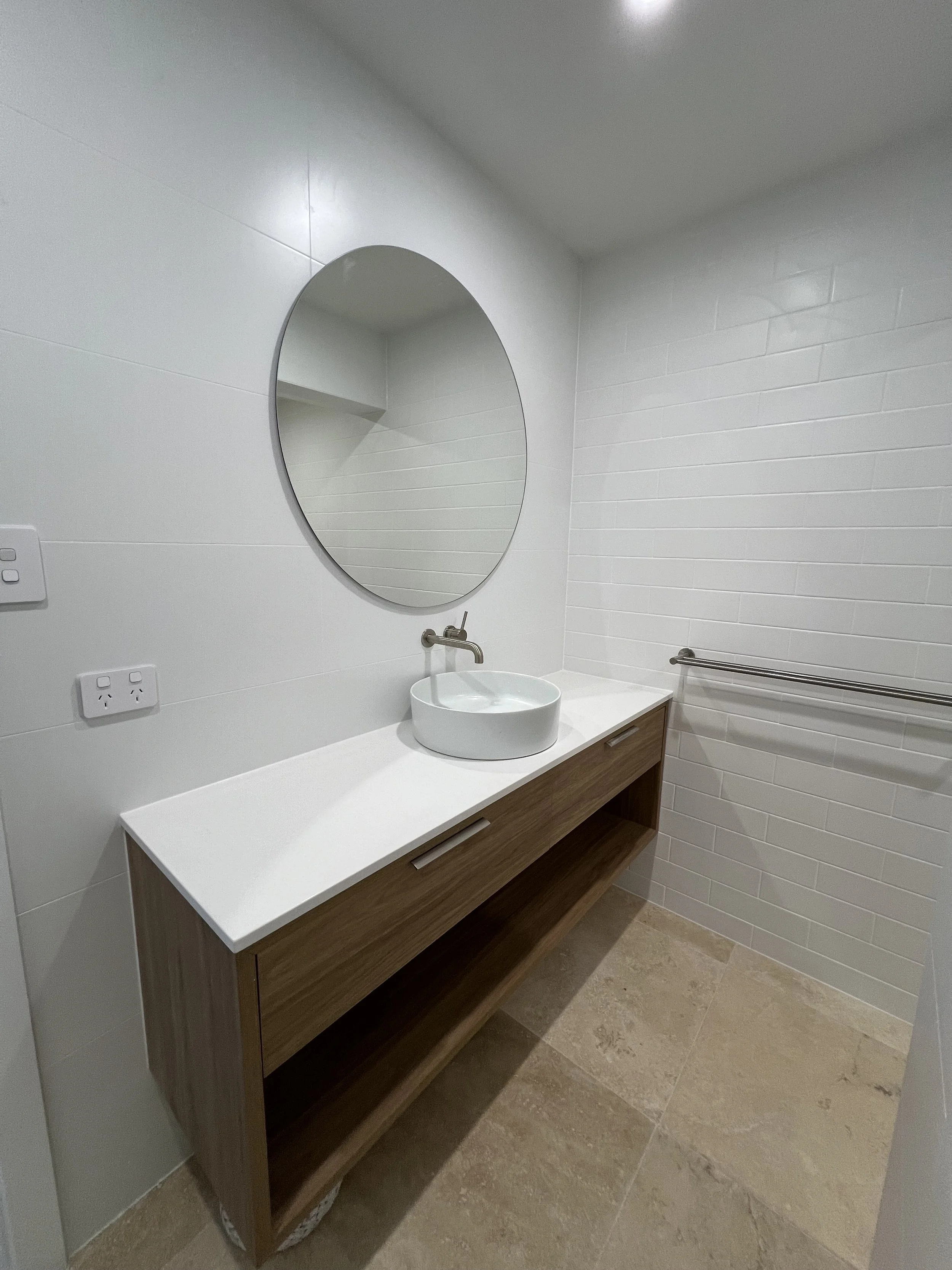 Modern bathroom with white walls, beige tile flooring, a white vanity to compliment granny flat by custom builder in western australia, with custom wooden shelving.