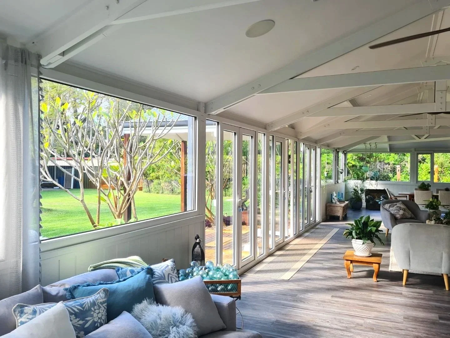Custom home build by local bussleton builders company, featuring bright sunroom with large windows and sliding glass doors opening to a garden with trees and lawn.