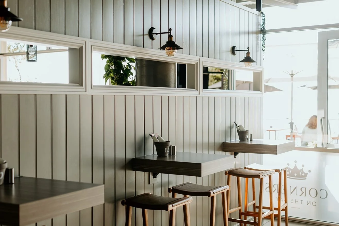 Interior of a café with wooden panel walls, bar-height tables with stools, and large windows letting in natural light.