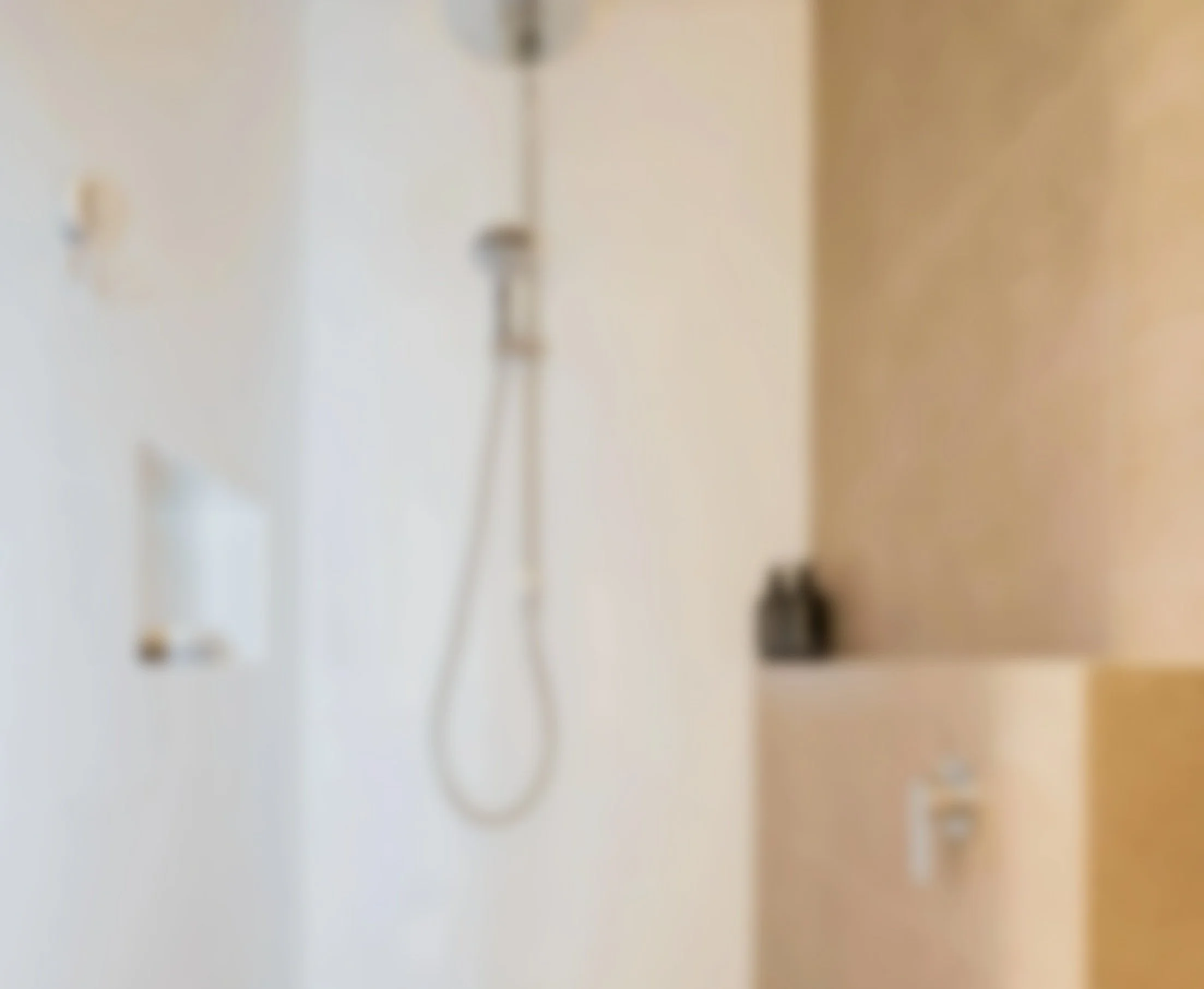 A blurry image of a shower area with a handheld showerhead attached to a white wall, and a partial view of a beige cabinet or shelf.
