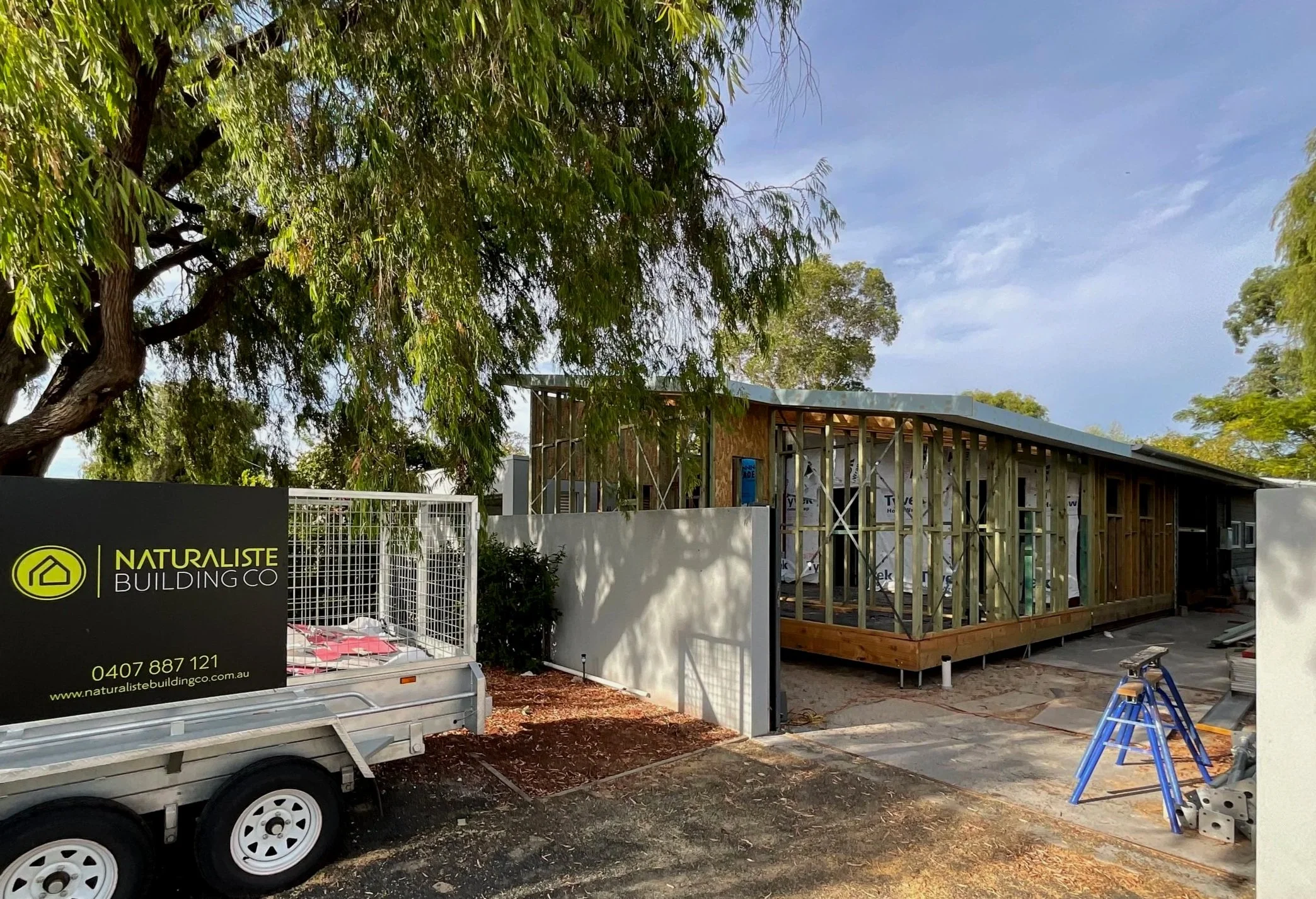 Construction site of a custom home build and home renovation in progress, with a sign that reads 'Naturaliste Building Co' and a trailer with construction materials.
