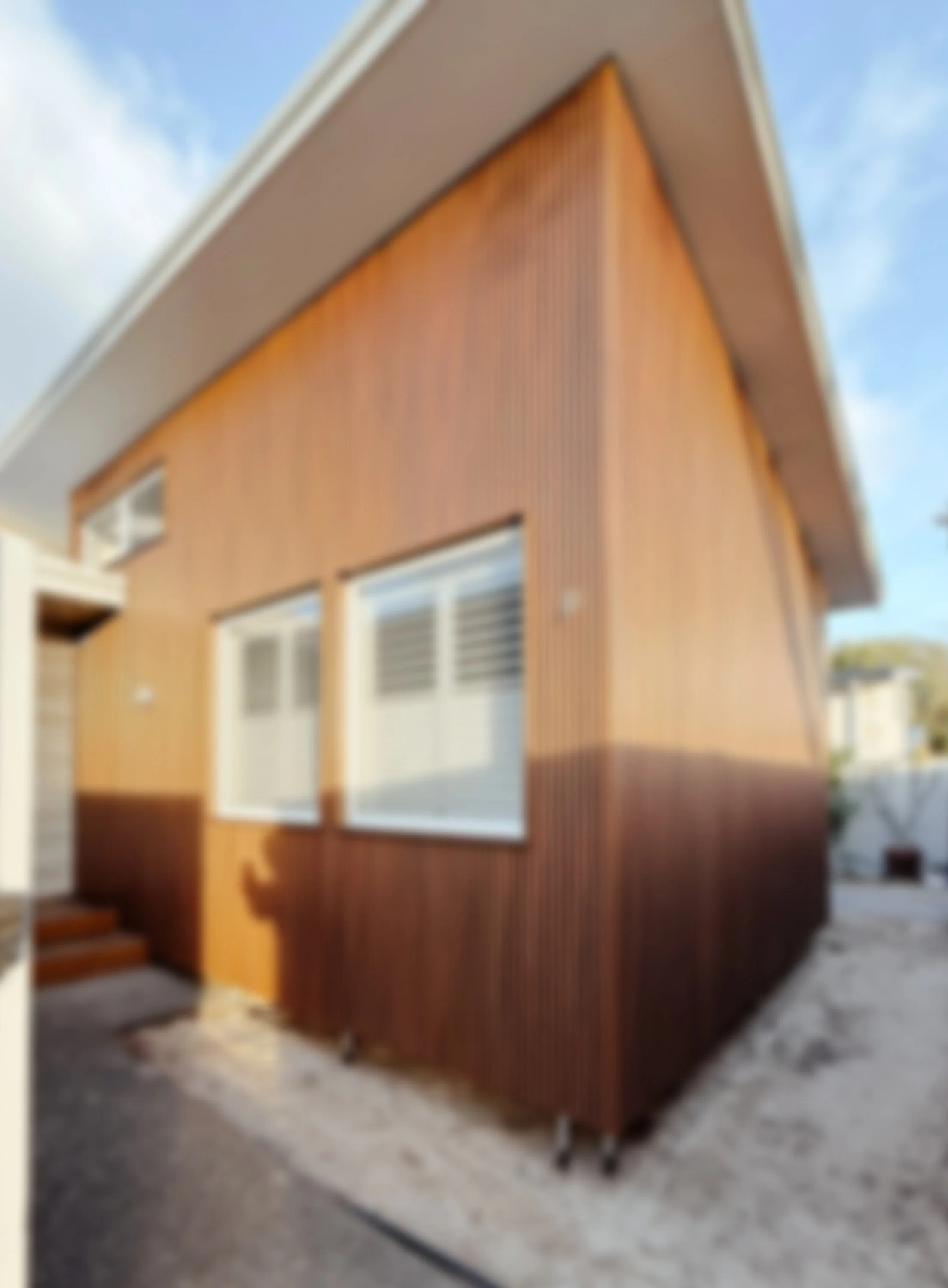 Blurry photo of a modern house exterior with wooden siding, two windows, and a small set of stairs leading to an entrance.