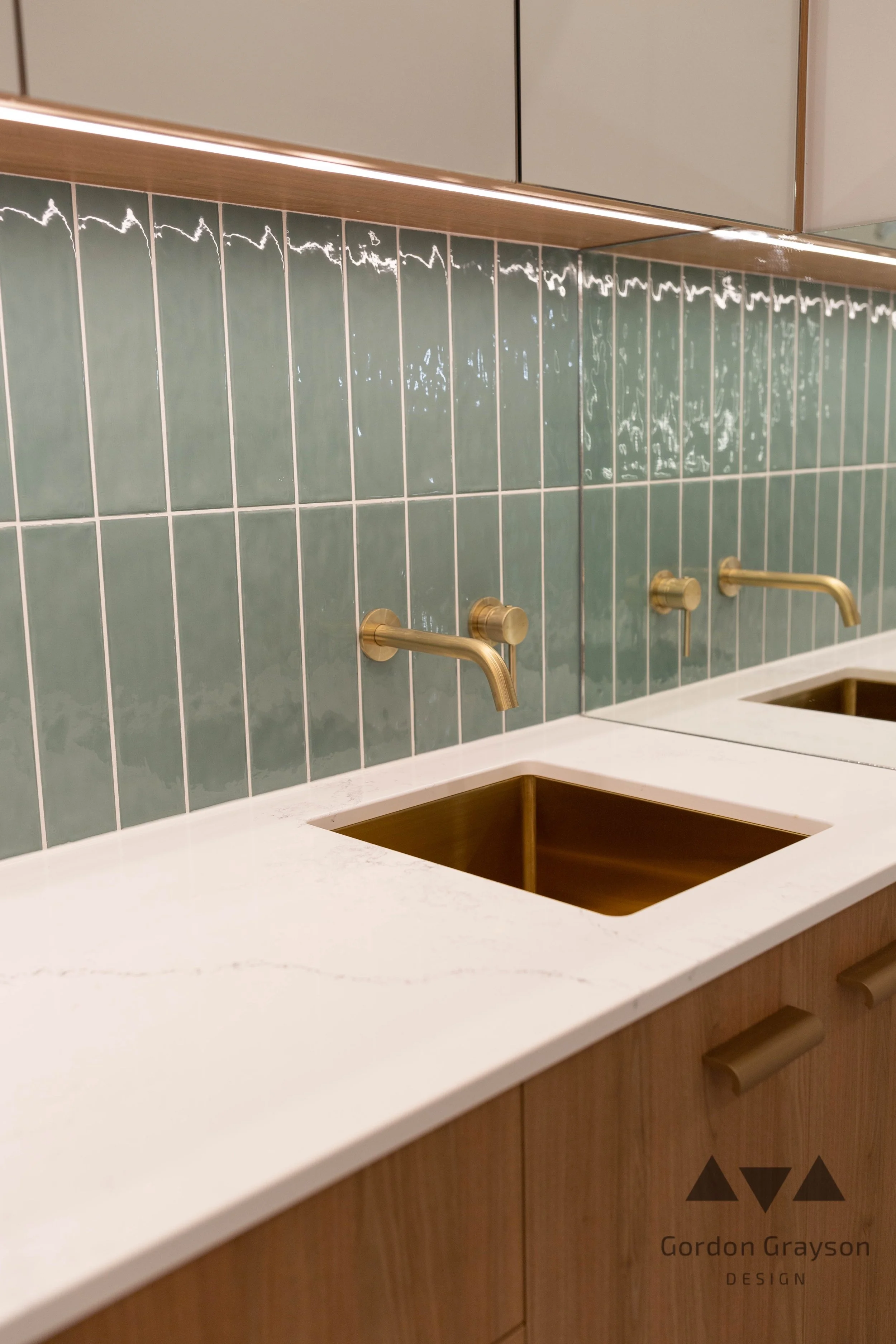 A modern bathroom sink area with a white marble countertop, two copper sinks, wall-mounted gold faucets for a commercial clinic custom design and build by local busselton builder