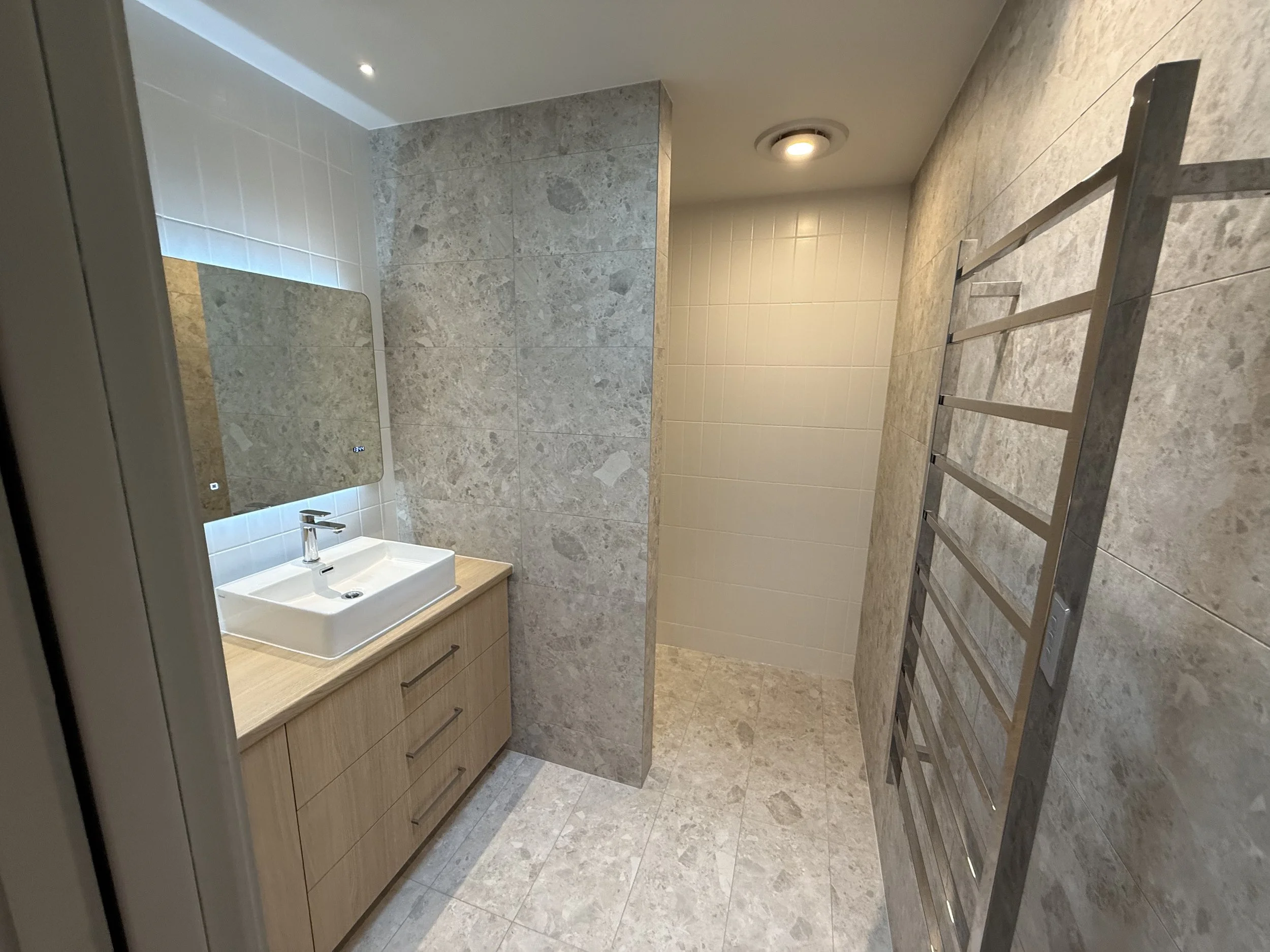 Modern bathroom with a wooden vanity, white rectangular vessel sink, large mirror, beige tile walls, metal towel rack, and a walk-in shower area in newly renovated homes yallingup
