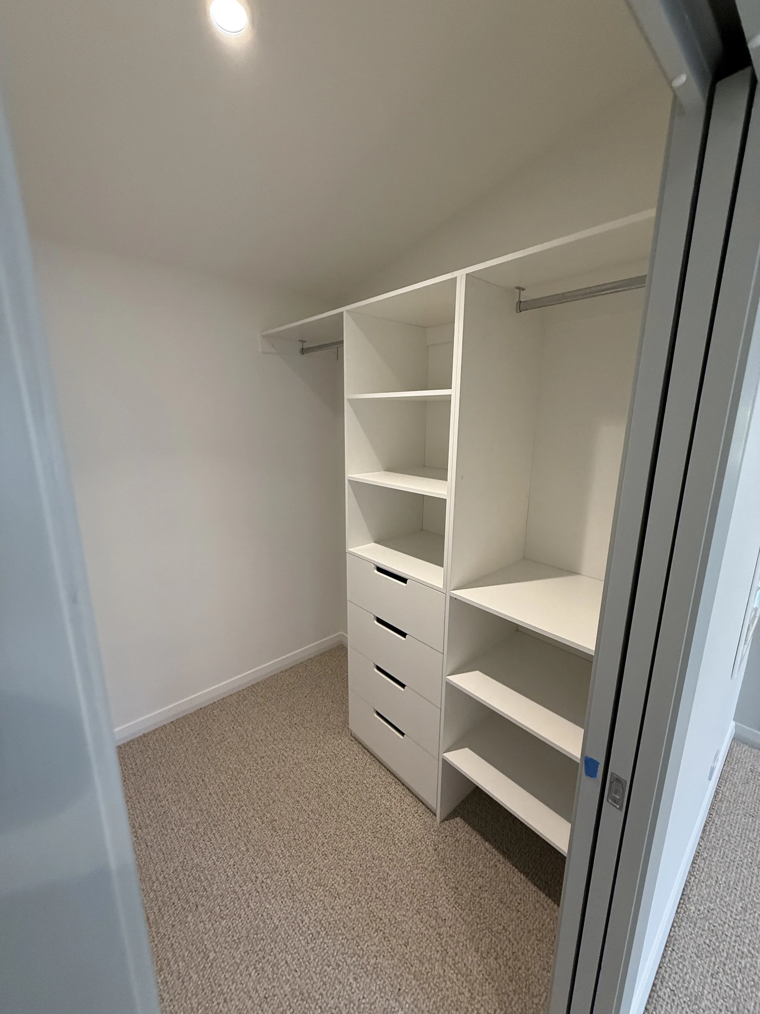 Empty walk-in closet with white built-in shelving and drawers, beige carpet, by custom home builders