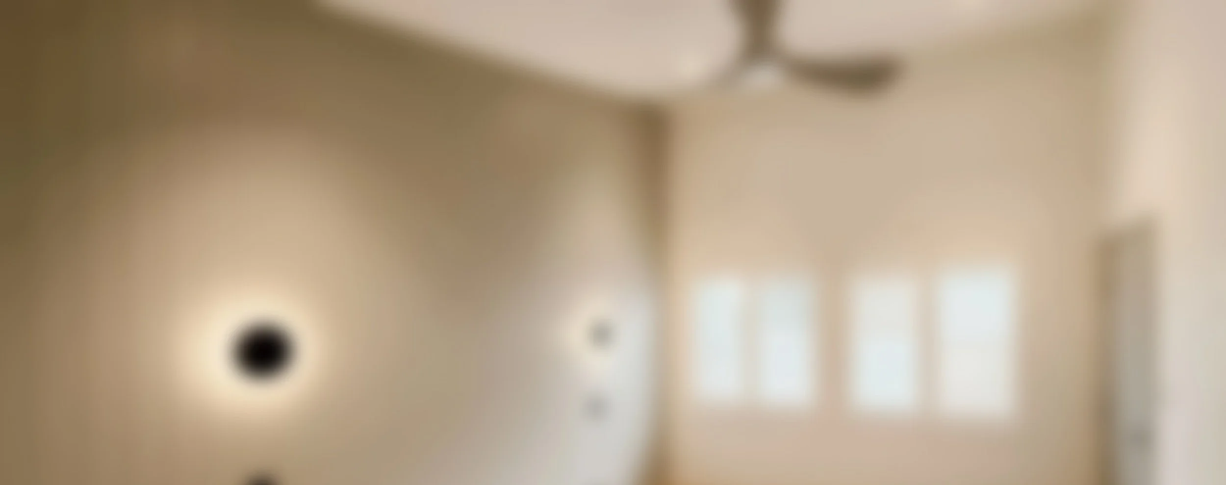 Blurred photo of a beige-colored room with windows and ceiling fans.