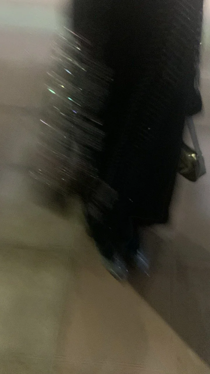 A blurry photo of a black suitcase or backpack on the floor next to a wall, with some reflection of lights on its surface.