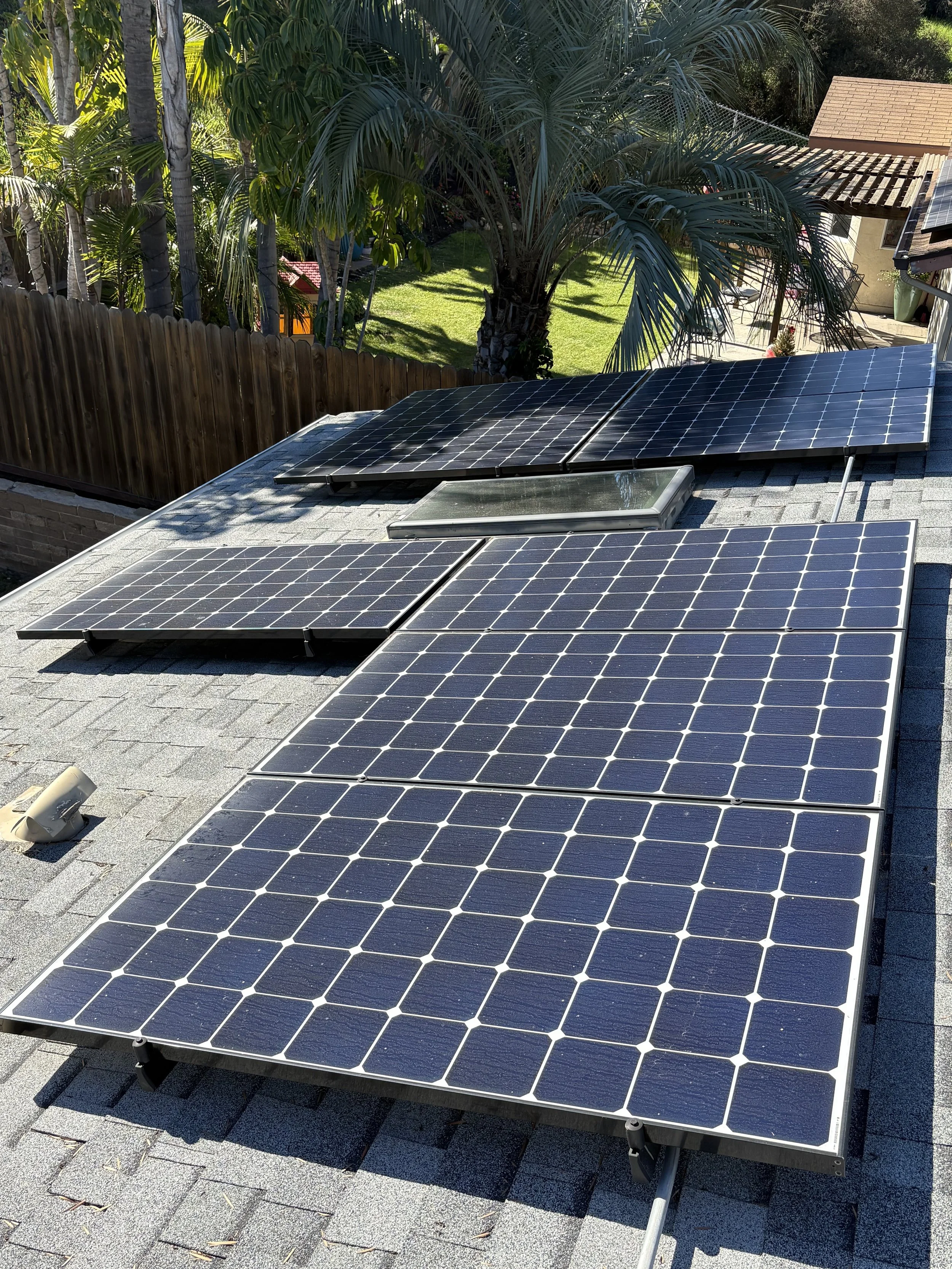 Multiple solar panels installed on a residential roof, with trees and a backyard visible in the background.