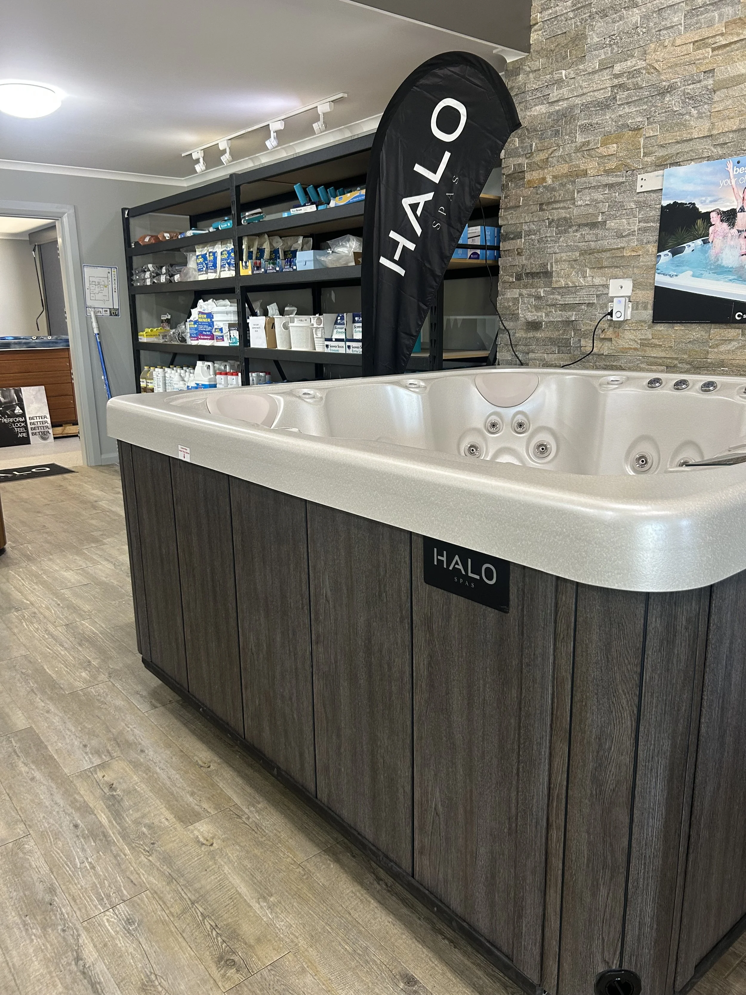Indoor hot tub with multiple jets at Halo Spas store, with shelves of spa supplies in the background.