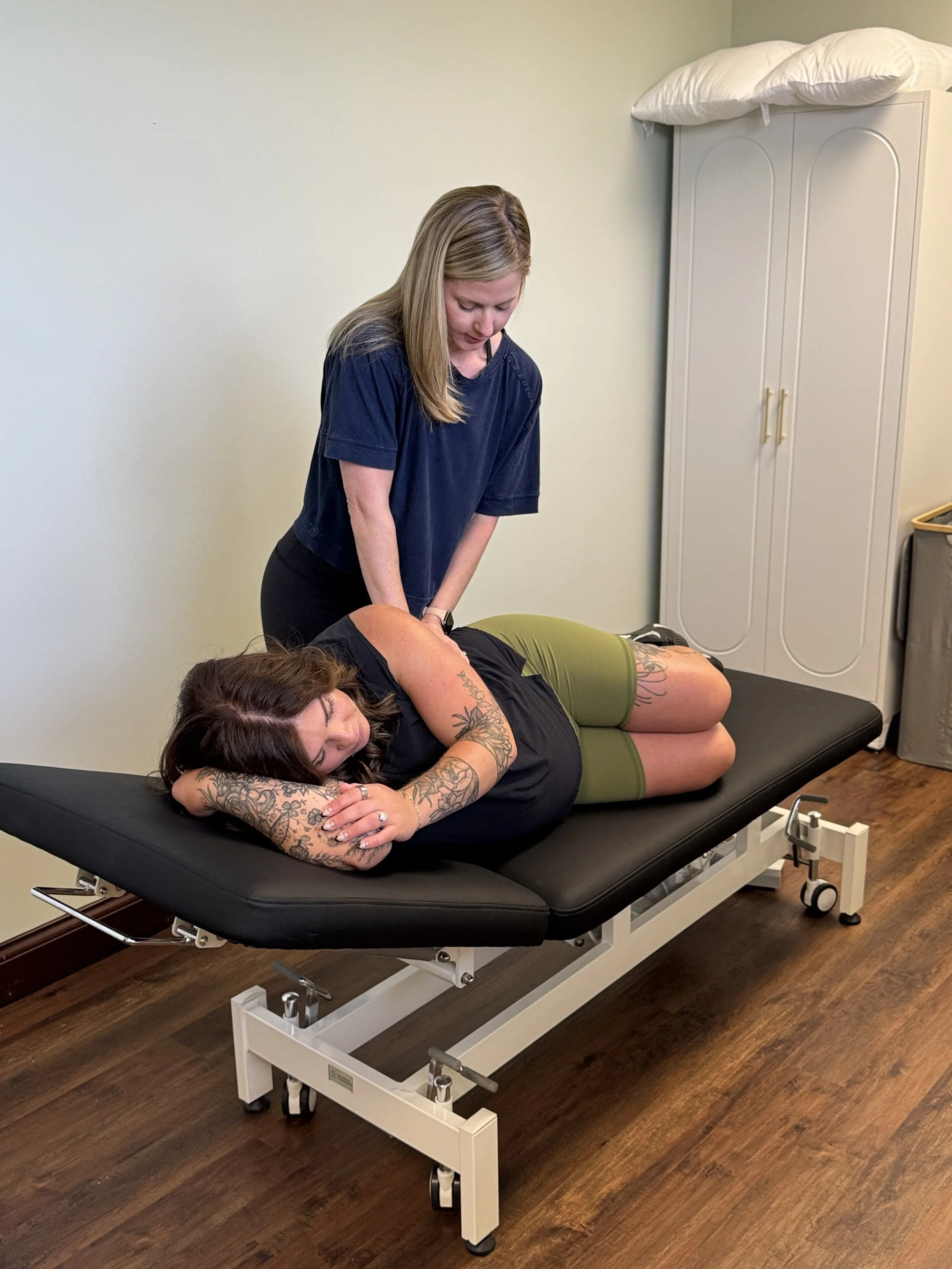 Pregnant woman practicing yoga on a mat in her living room with houseplants and large windows in the background.