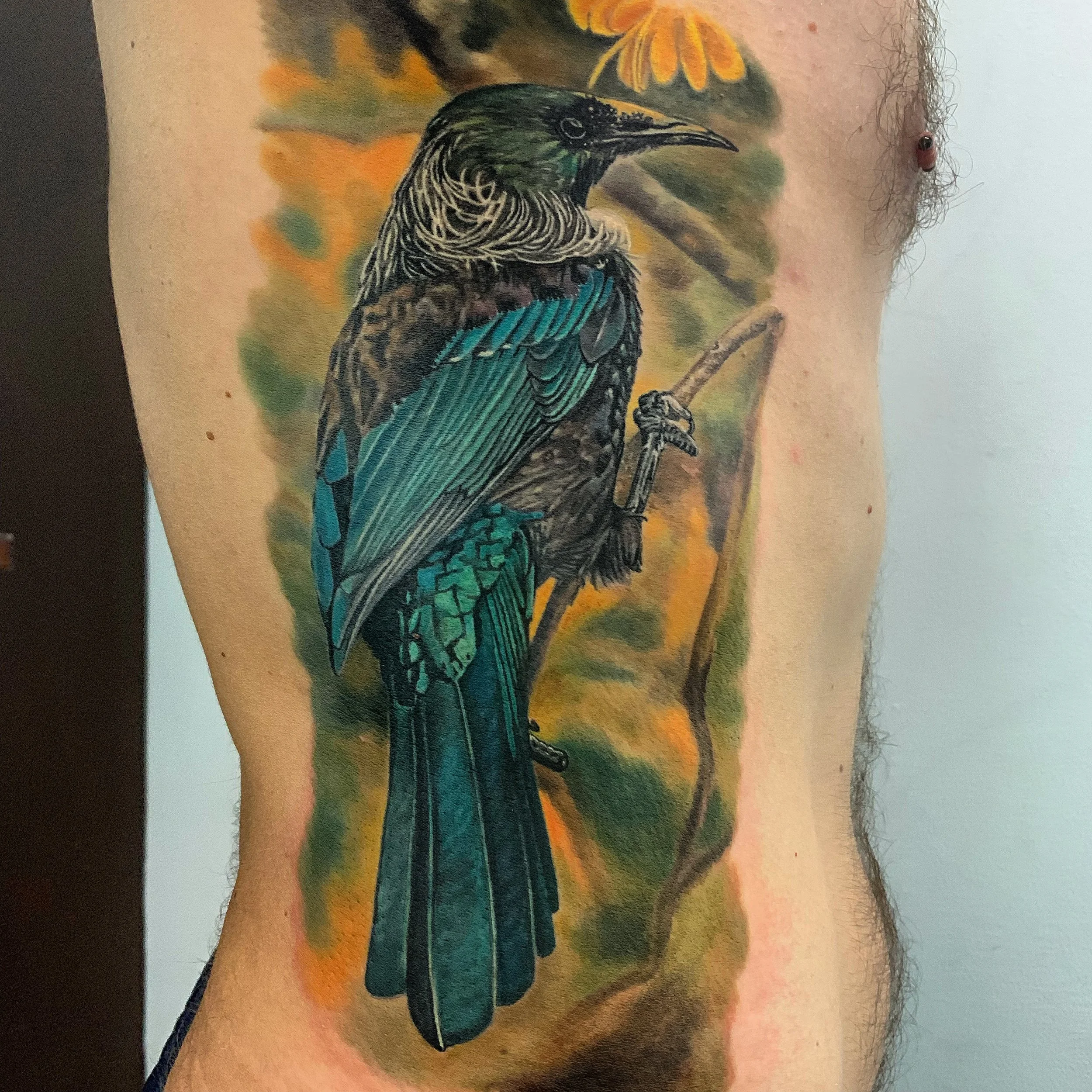Colorful tattoo of a bird perched on a branch on a person's side