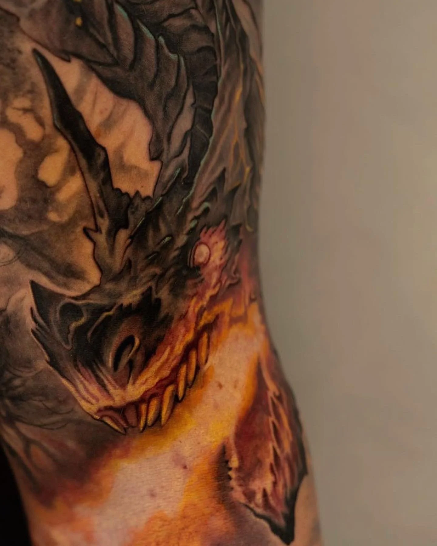 Close-up of a detailed tattoo on a person's shoulder and upper arm, featuring a menacing skull with sharp teeth, flames, and dark, fiery colors.