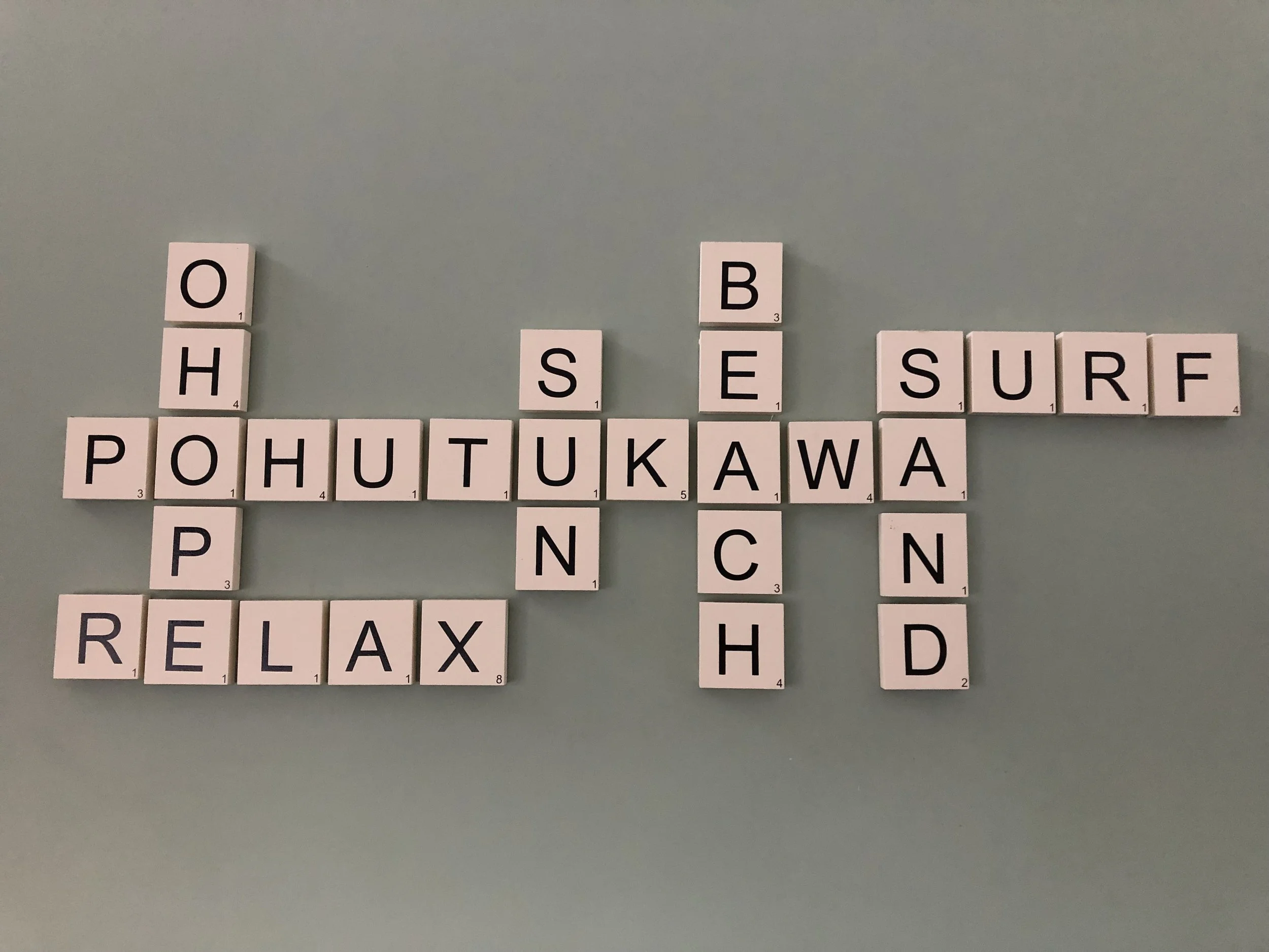 Crossword puzzle with words related to surfing and relaxation, including 'OHIO', 'SAND', 'SURF', 'RELAX', and names like 'POHUTUKAWA' and 'TUKAWA' arranged on a light green background.