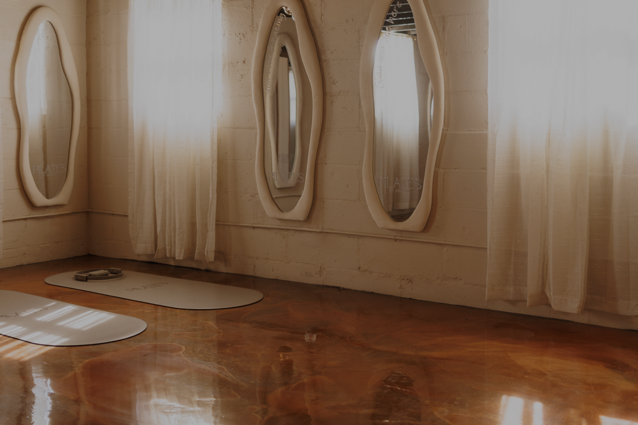 Sunlit Pilates studio with reformer mats on a wooden floor, sheer curtains, and a smartphone mockup displayed on the right side