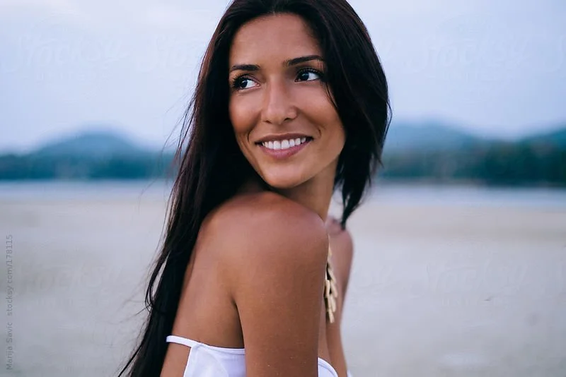 Image of a woman on the beach looking over her shoulder and smiling joyfully into the distance