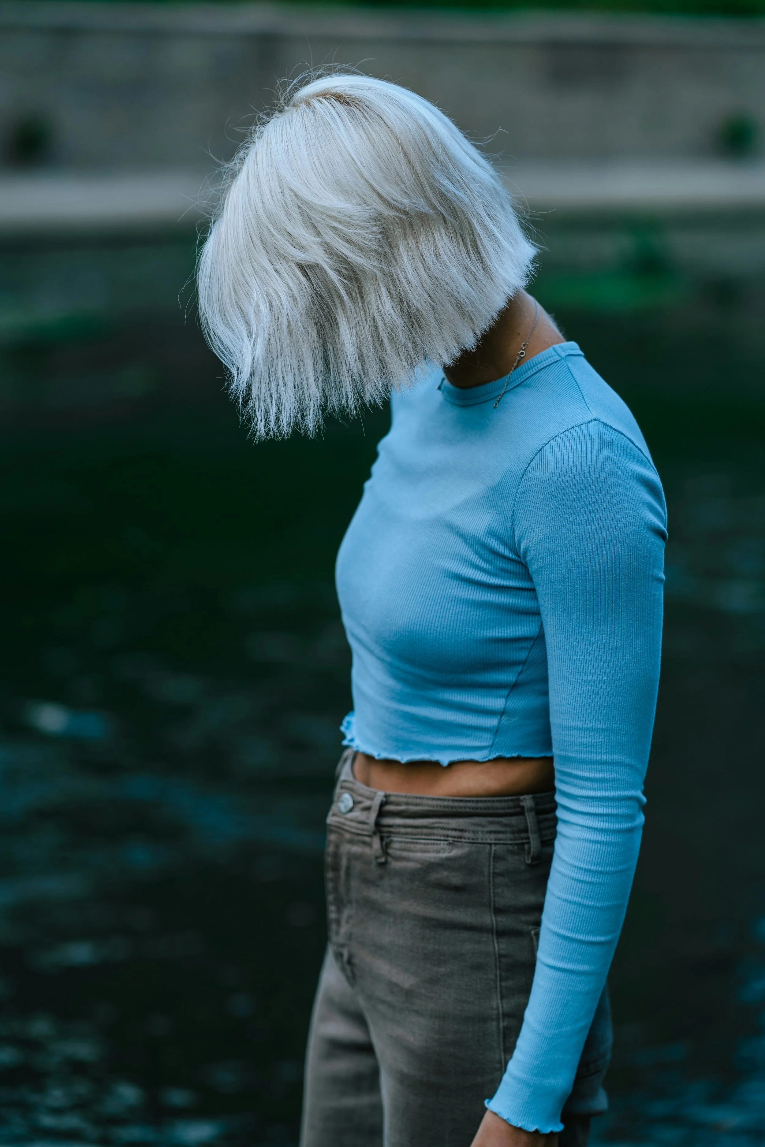 Image of a woman in a blue crop top displaying a flat abdomen and walking thoughtfully along a river