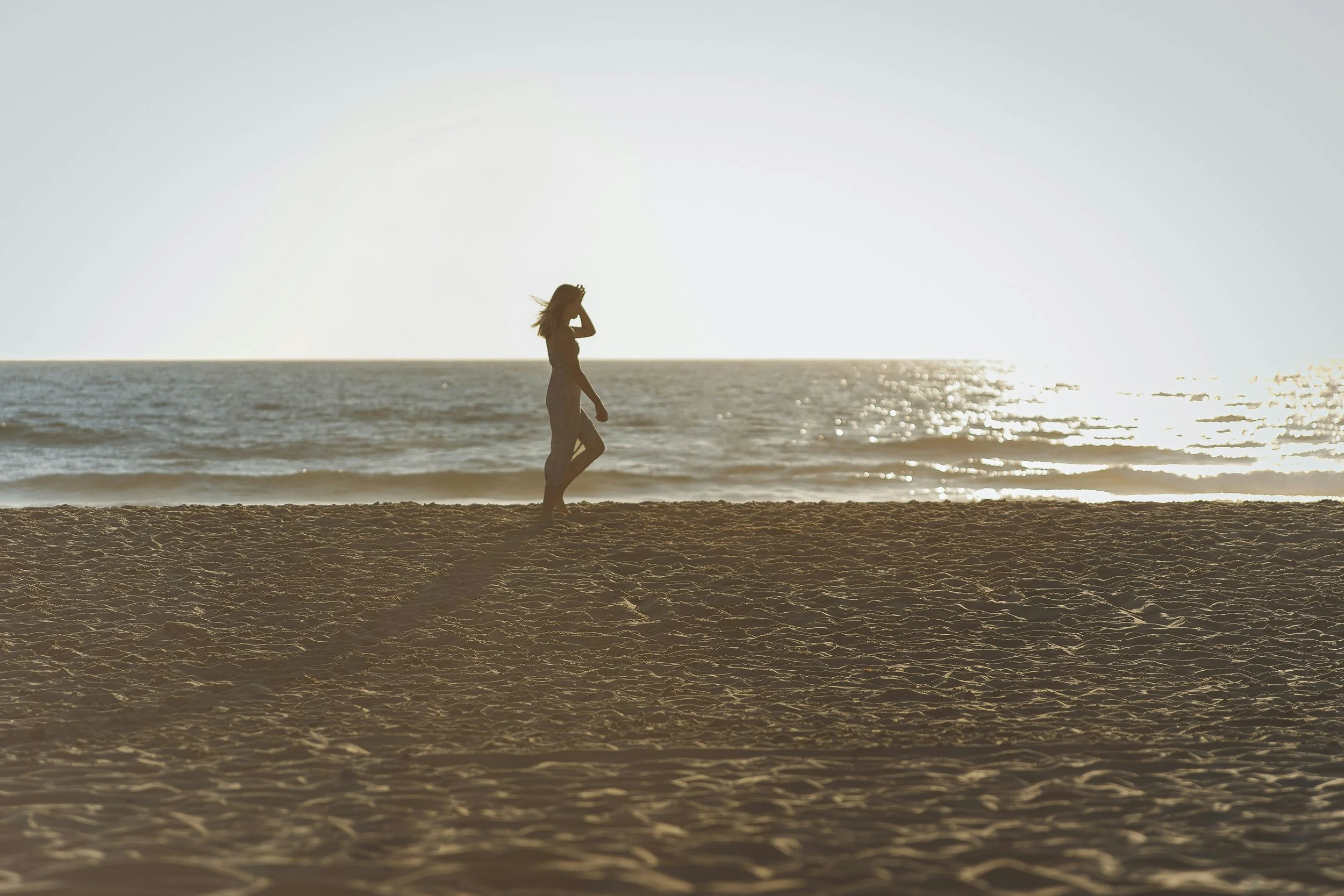 Image of woman walking in a long dress along the beach at sunrise