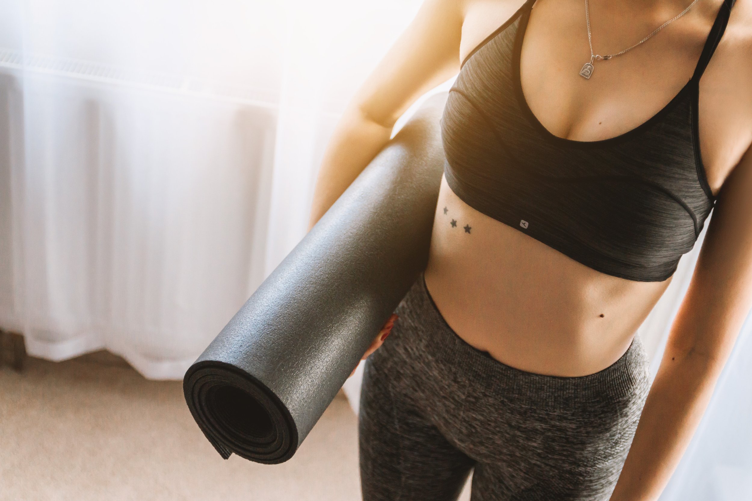 Image of a woman in a black sports bra and workout pants, holding a black yoga mat