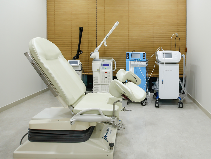 Medical equipment in a laboratory or hospital setting, including a large, white, robotic machine with a circular component and a screen, surrounded by chairs and other devices.