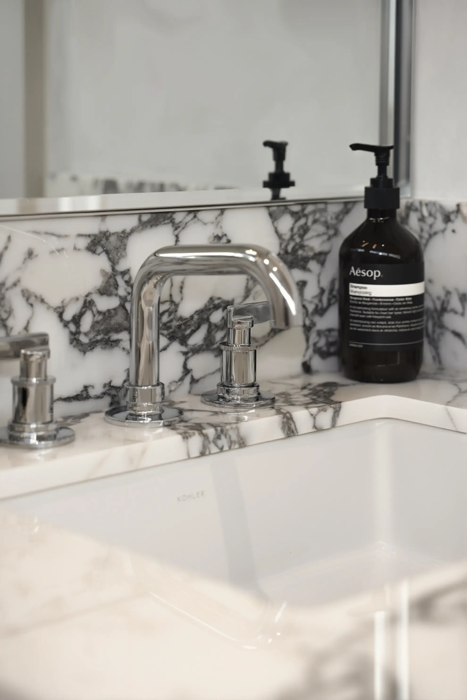 Luxury powder room in Toronto designed by Claire Design Studio, featuring a bespoke thick-edge marble vanity with dramatic veining, modern minimalist pendant lighting, and warm natural sunlight.