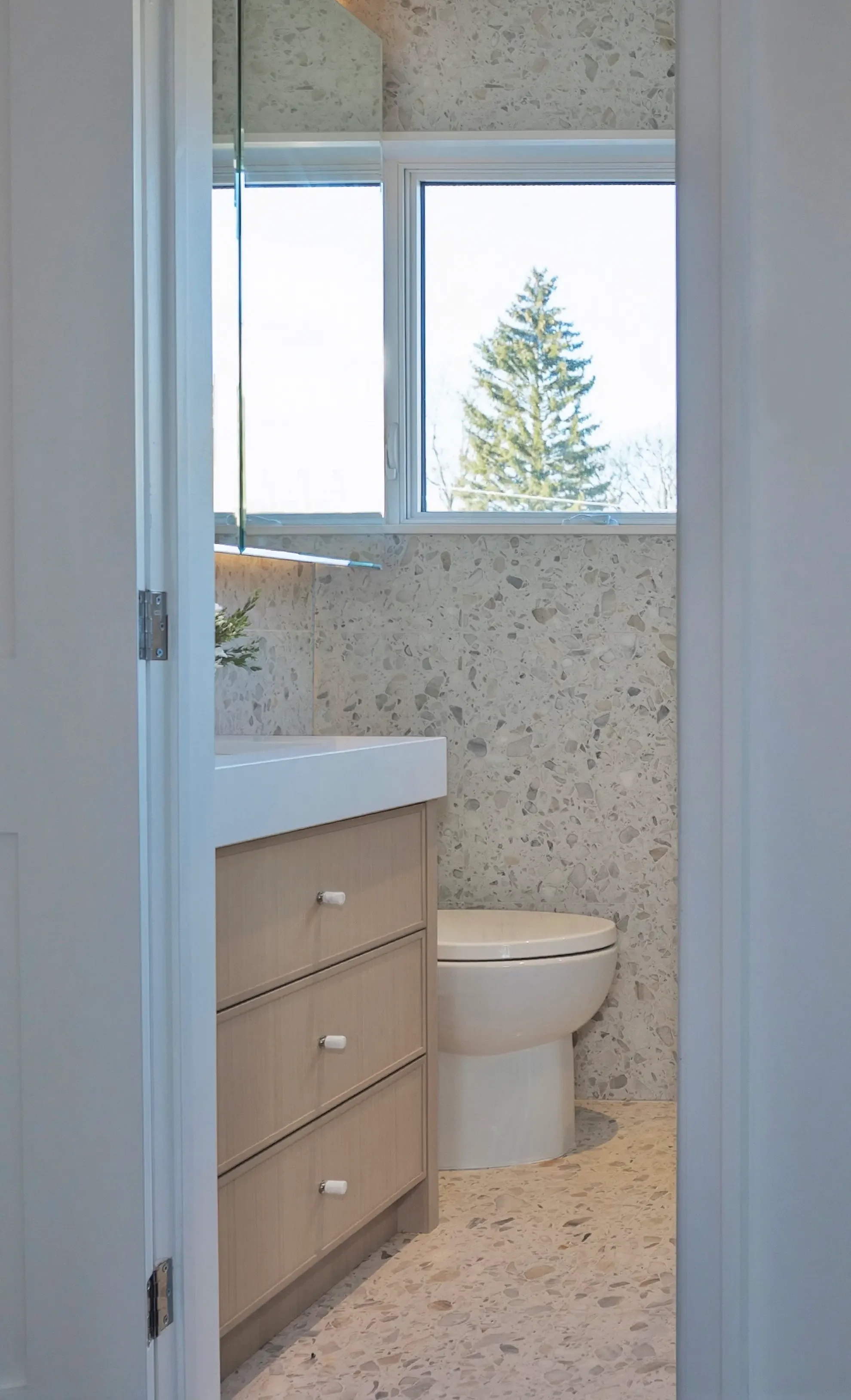 Modern organic bathroom in Toronto designed by Claire Design Studio, featuring full-height terrazzo wall tiles, a bespoke light oak vanity with white stone countertop, and integrated under-cabinet lighting.
