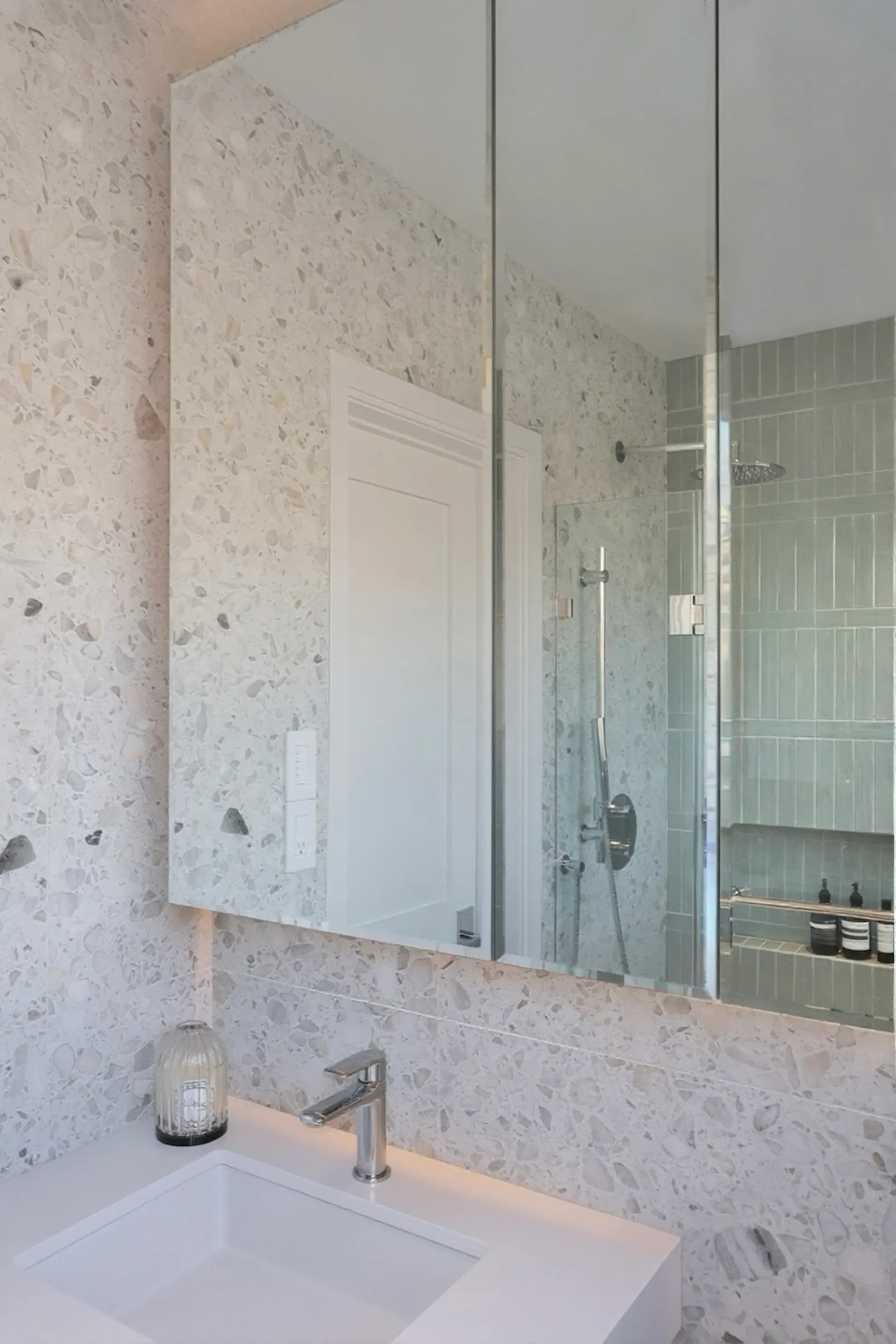 Modern kids bathroom in Toronto designed by Claire Design Studio, featuring full-height terrazzo wall tiles, a large mirrored medicine cabinet, and a walk-in shower with vertical sage green tiles.