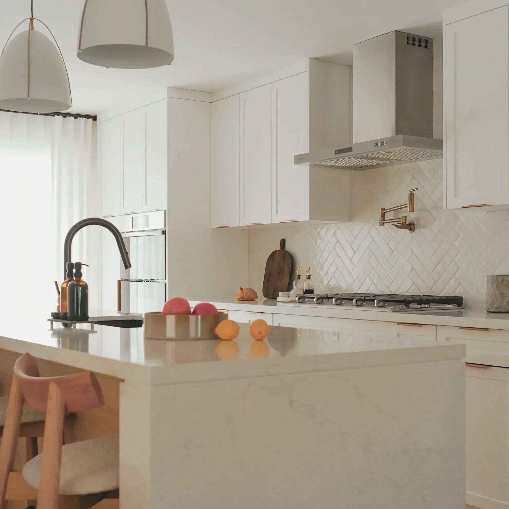 Modern white kitchen in Toronto designed by Claire Design Studio featuring a white herringbone tile backsplash, quartz countertops, and a professional-grade range hood.