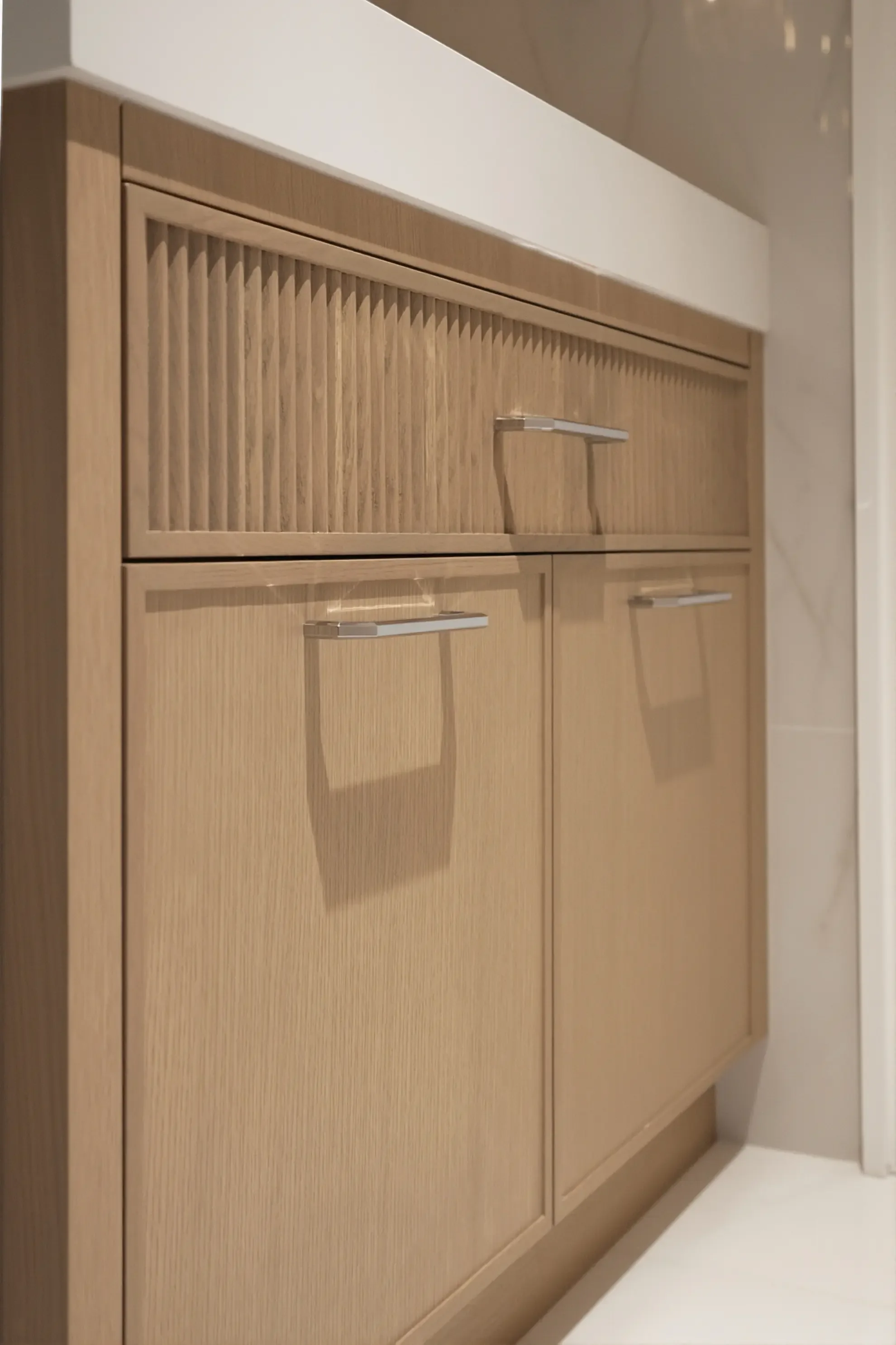 Detailed view of a custom light wood bathroom vanity in Toronto by Claire Design Studio, featuring a fluted upper drawer, Shaker-style lower cabinets, and modern polished chrome hardware.