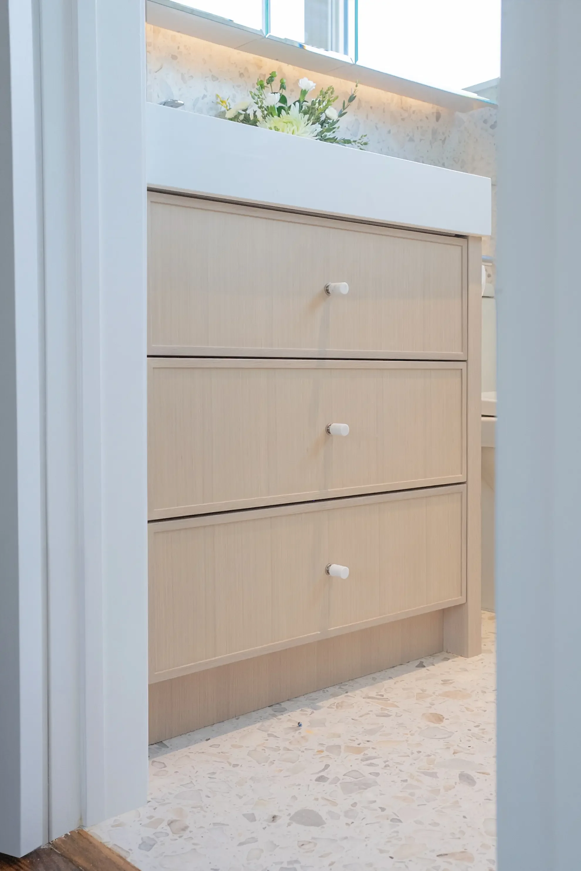 Bespoke light oak bathroom vanity with minimalist marble knobs and a thick white countertop, paired with a modern terrazzo tile floor, designed by Claire Design Studio in Toronto.