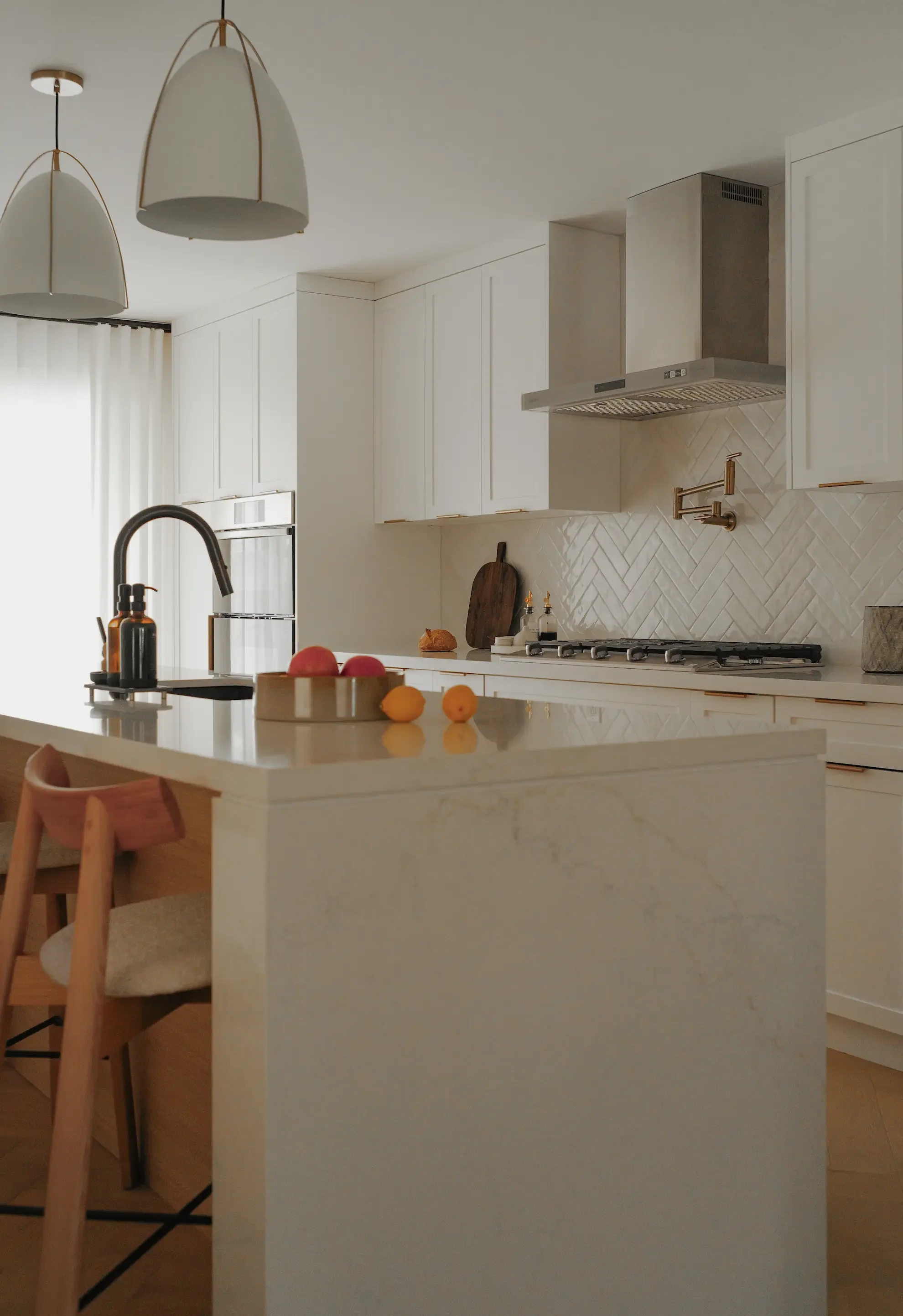 Modern white kitchen in Toronto designed by Claire Design Studio featuring a white herringbone tile backsplash, quartz countertops, and a professional-grade range hood.