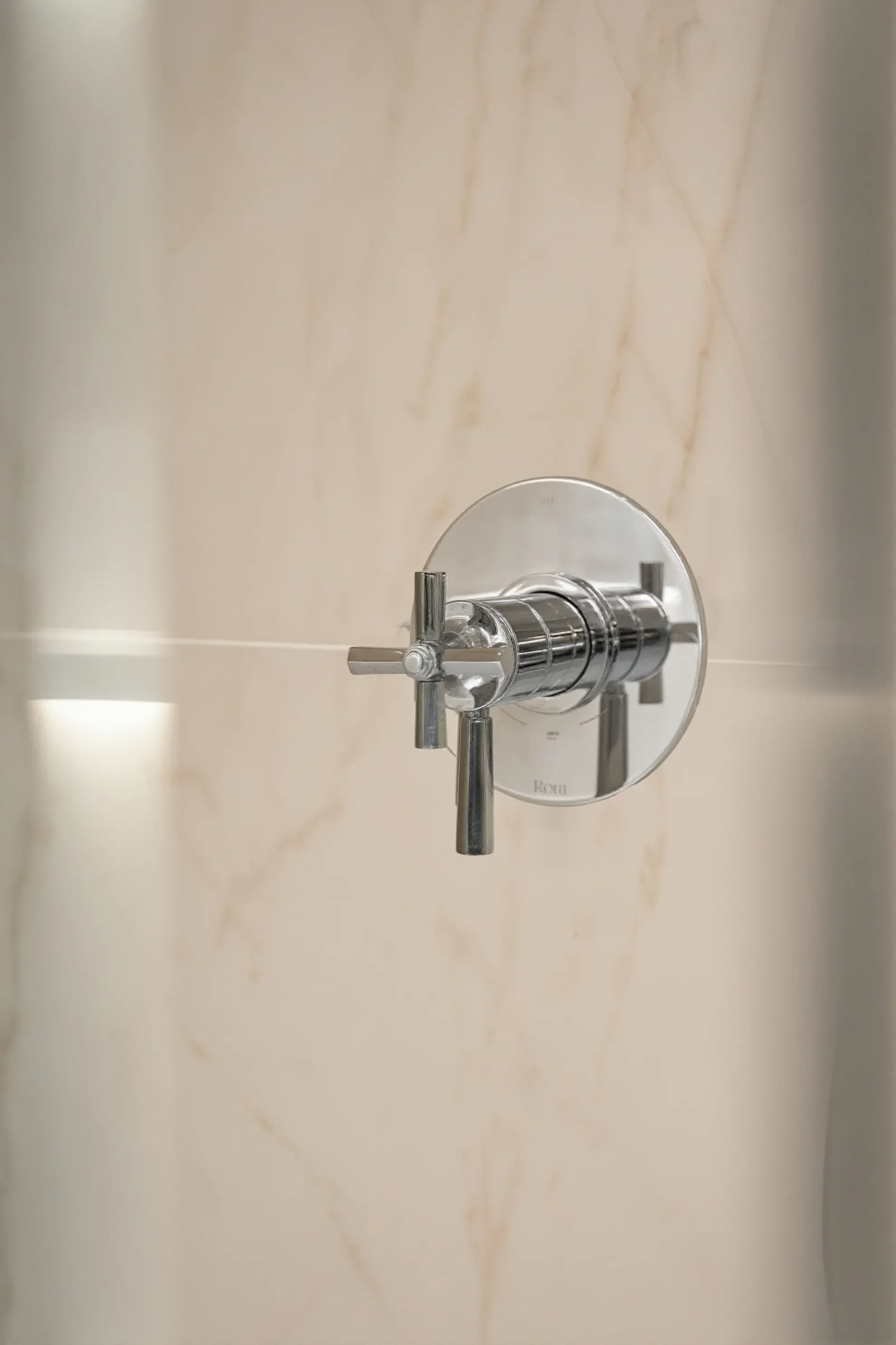 Close-up detail of a polished chrome cross-handle shower thermostatic valve installed against a marble slab wall in a Toronto residential project by Claire Design Studio.